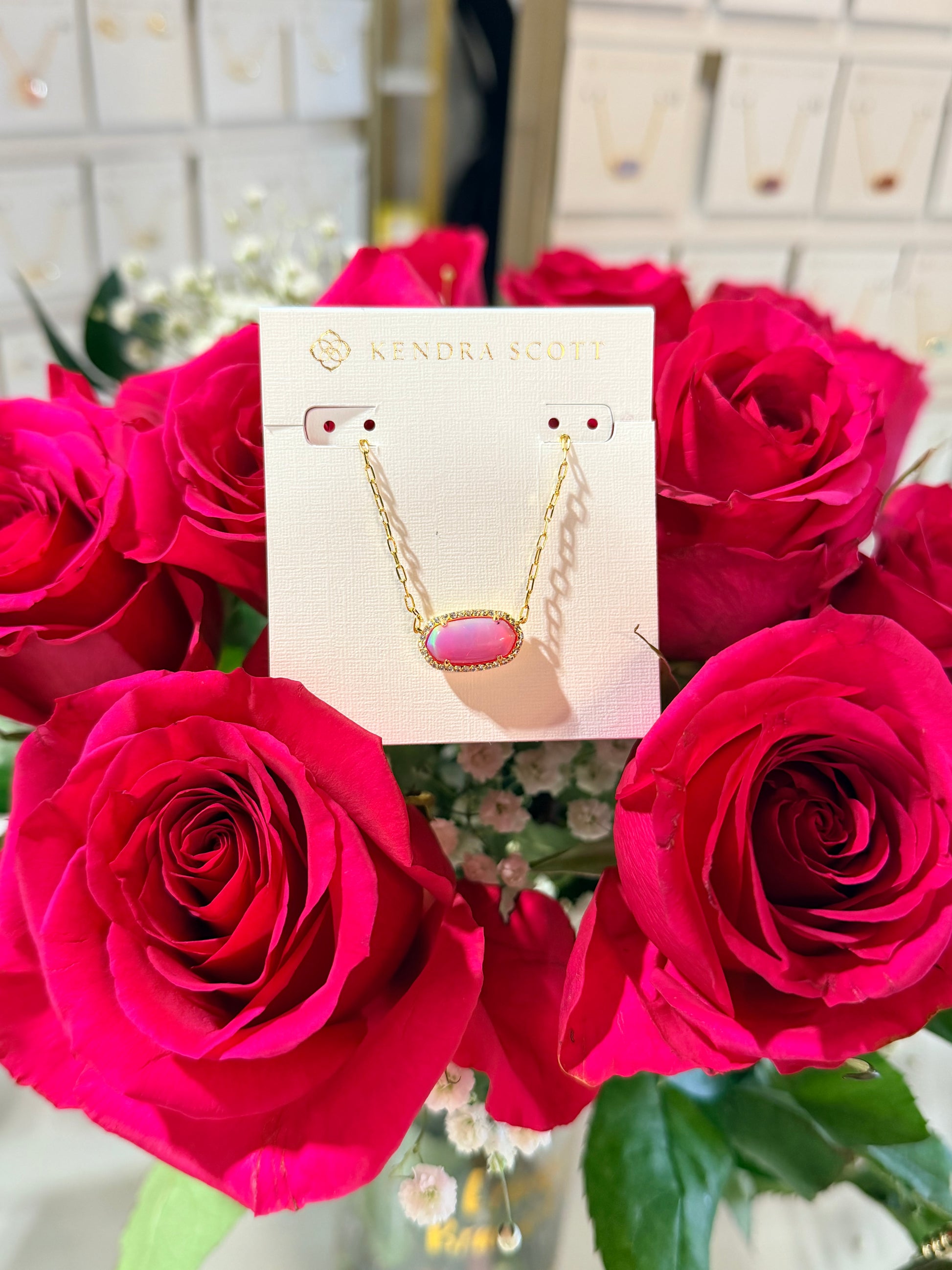 Necklace card with a pink pendant displayed among red roses.