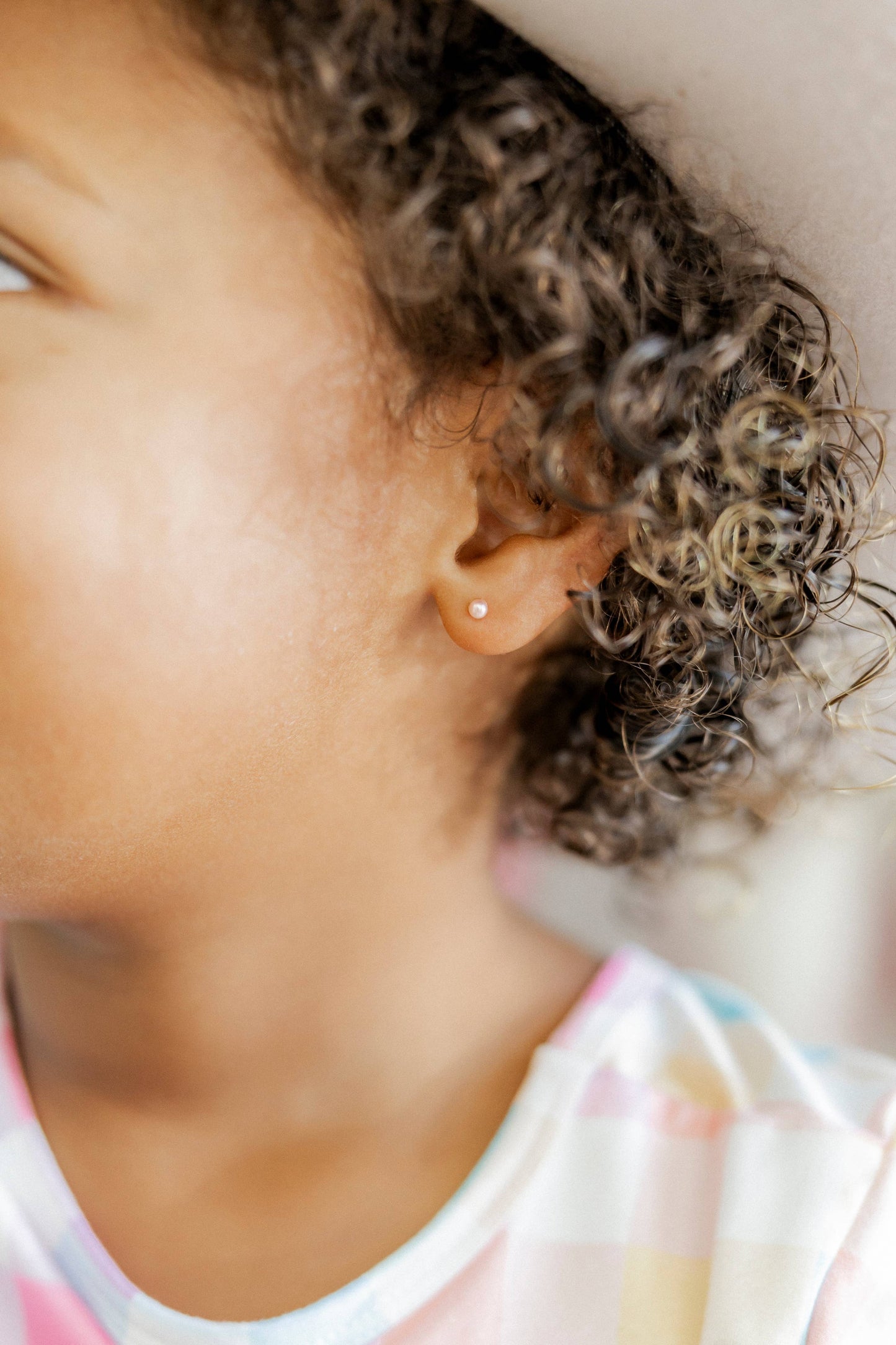 Close-up of a child's ear with an earring, wearing a colorful shirt.