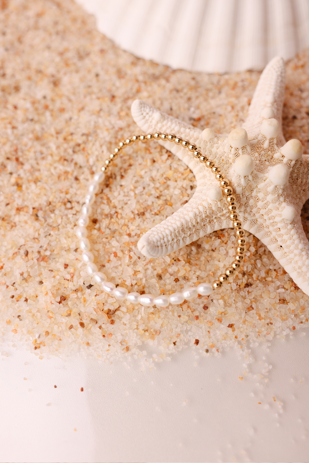 Gold bracelet on sand with a starfish and shell in the background