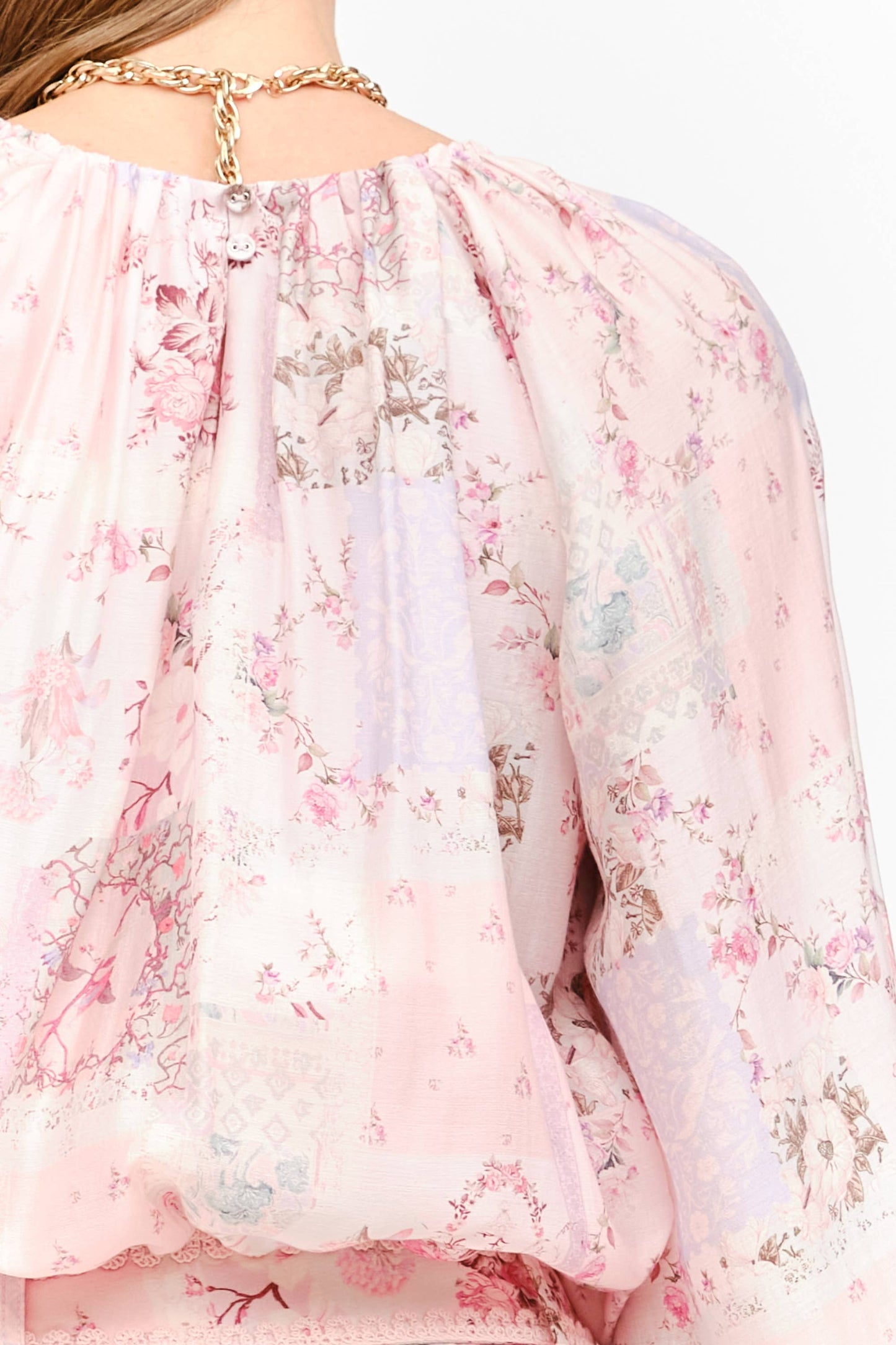Close-up of a light pink floral blouse with a delicate floral print, featuring a high neckline with a gold chain detail.