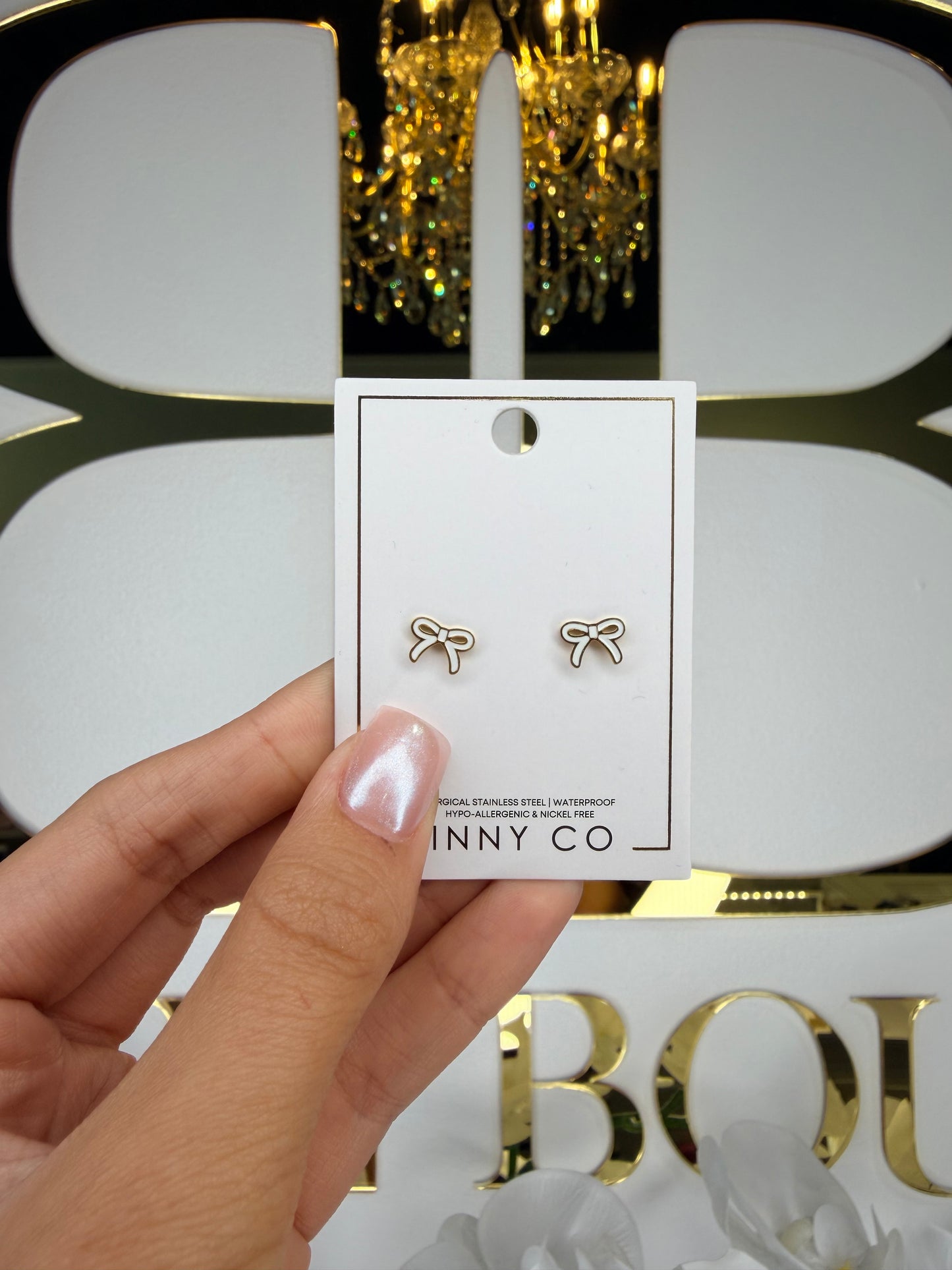 Hand holding a card with gold bow-shaped earrings in front of a decorative background