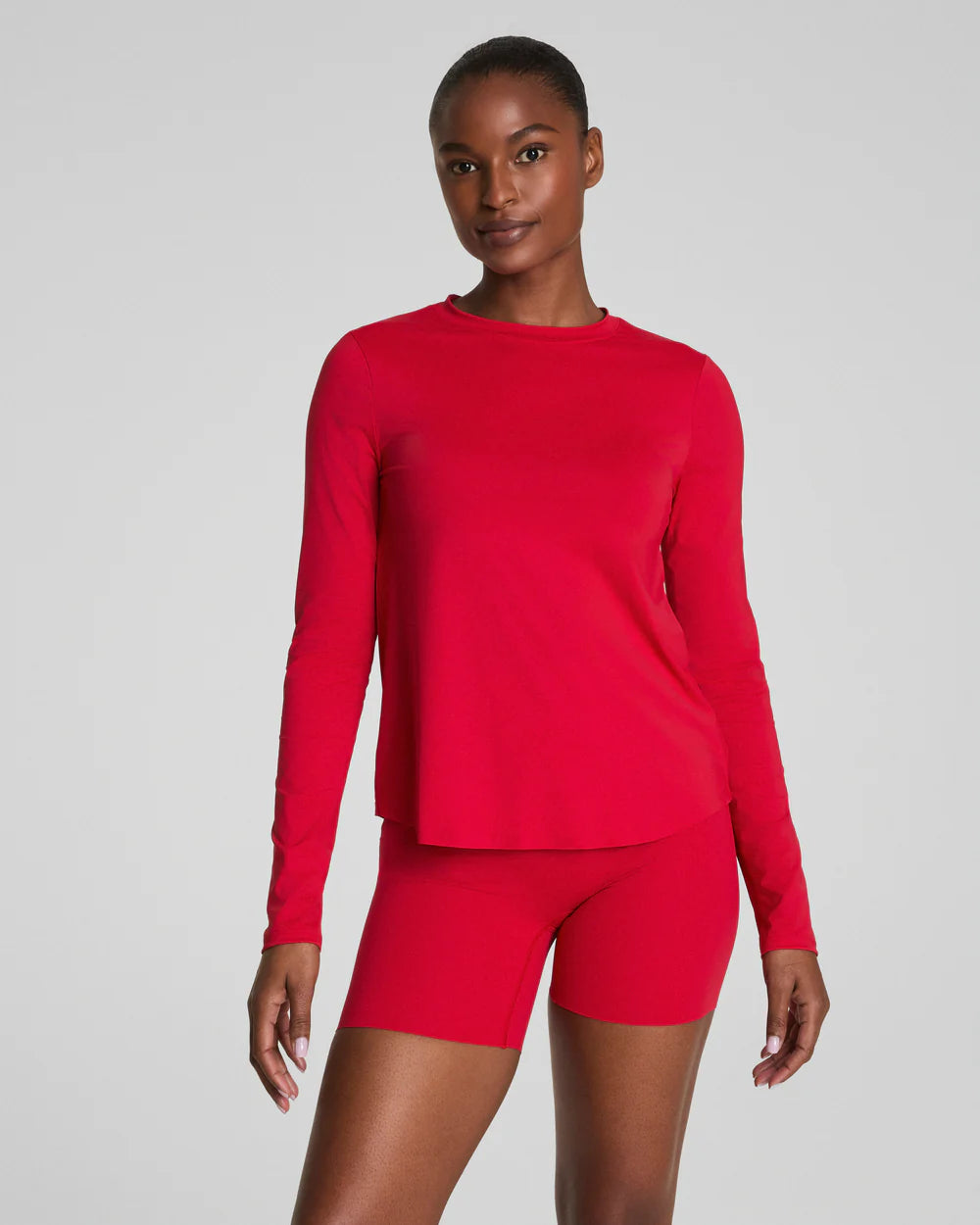 Person wearing a red long-sleeve top and shorts on a gray background