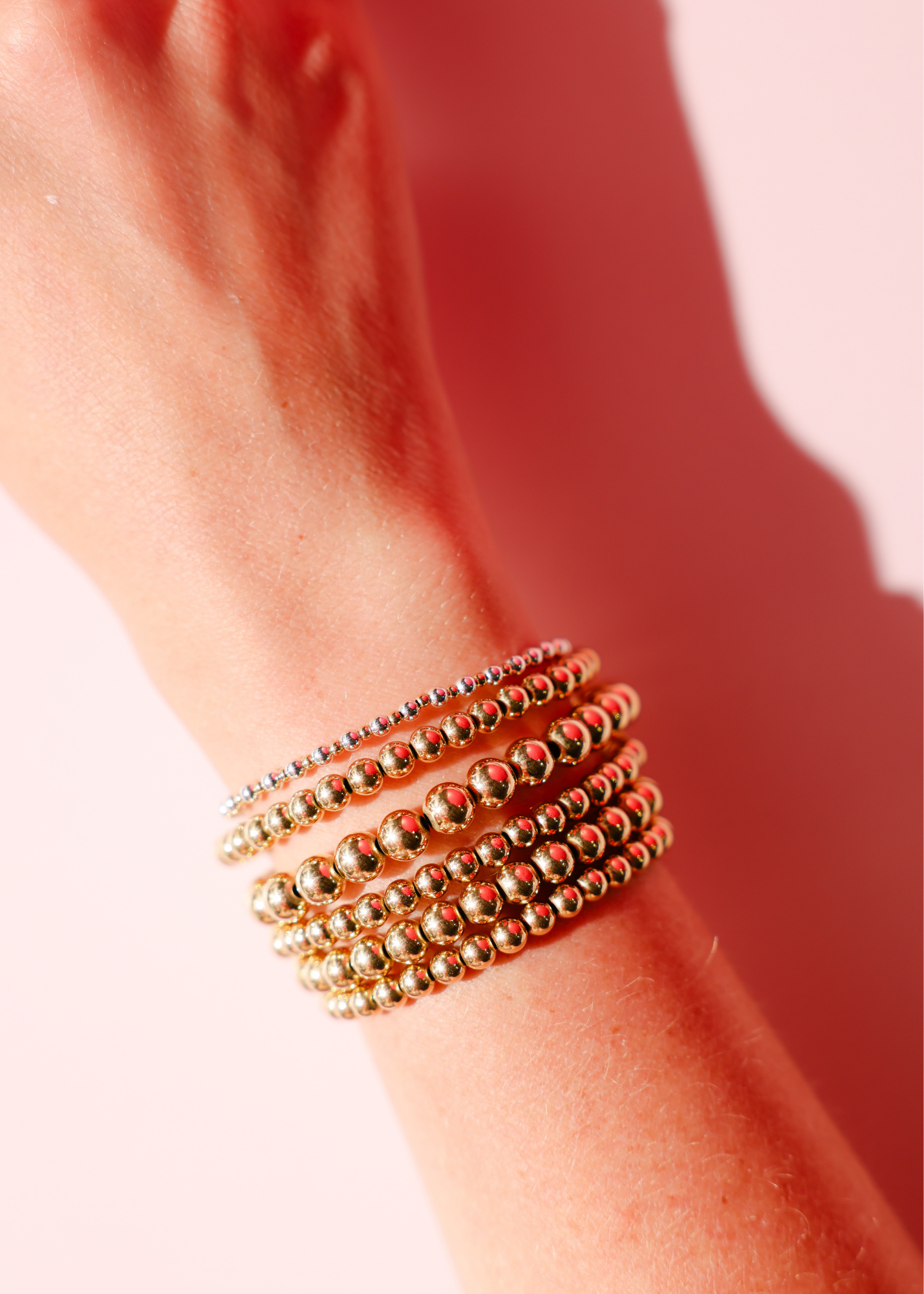Gold beaded bracelets on a wrist with a soft pink background