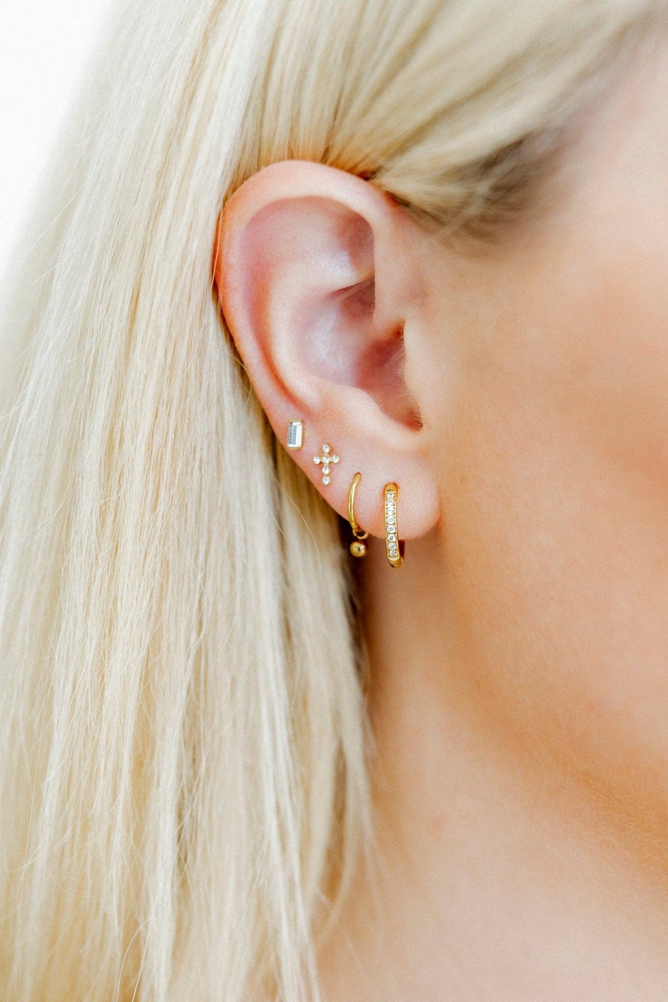 Close-up of an ear wearing gold hoop earrings with a blurred background