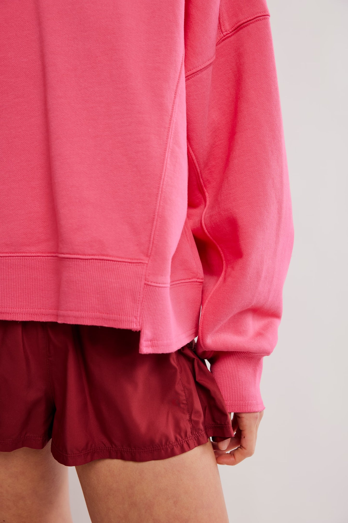 Person wearing a pink sweatshirt and maroon shorts on a light background