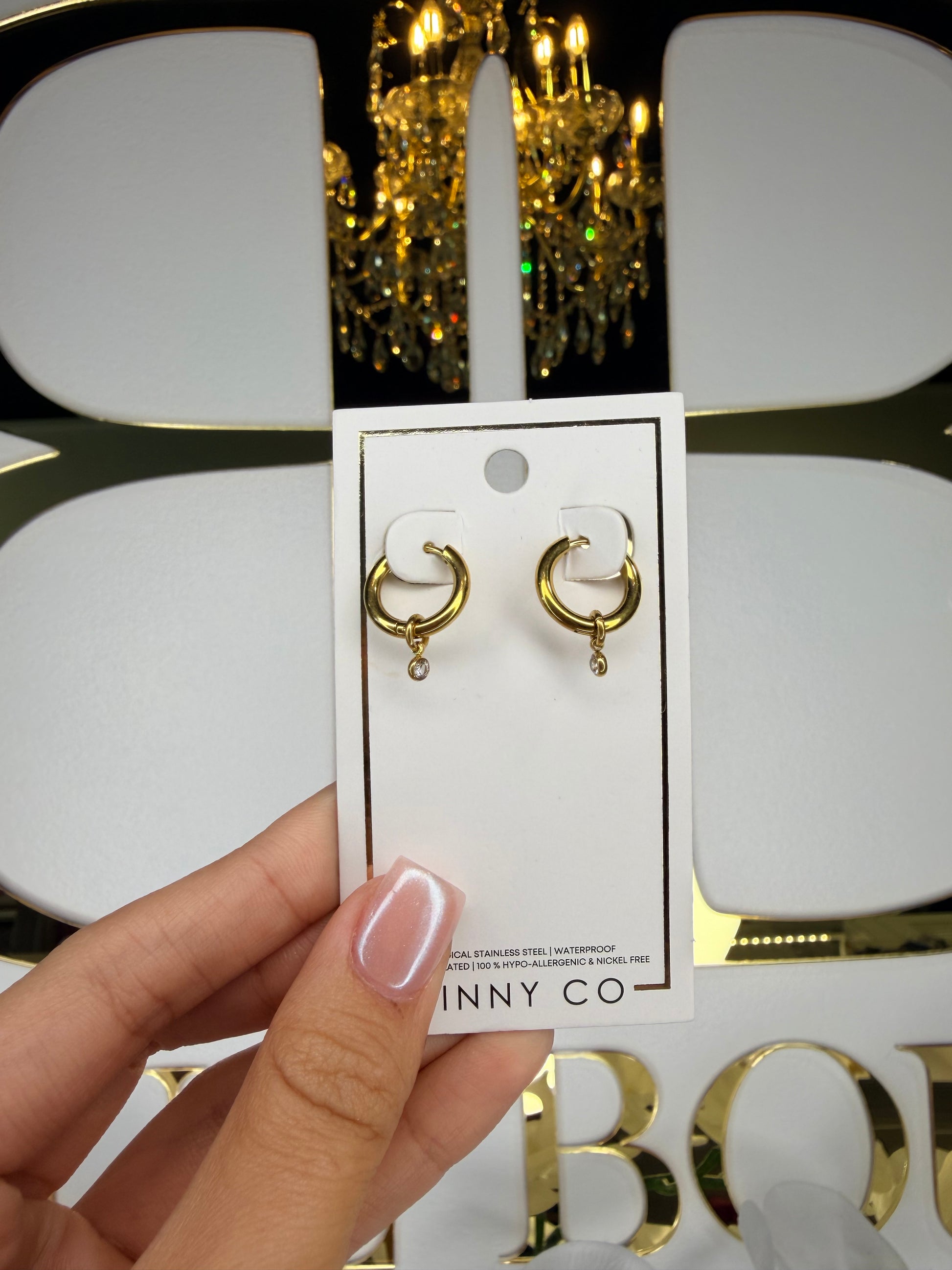 Gold earrings held above a white box with 'INNY CO' branding.