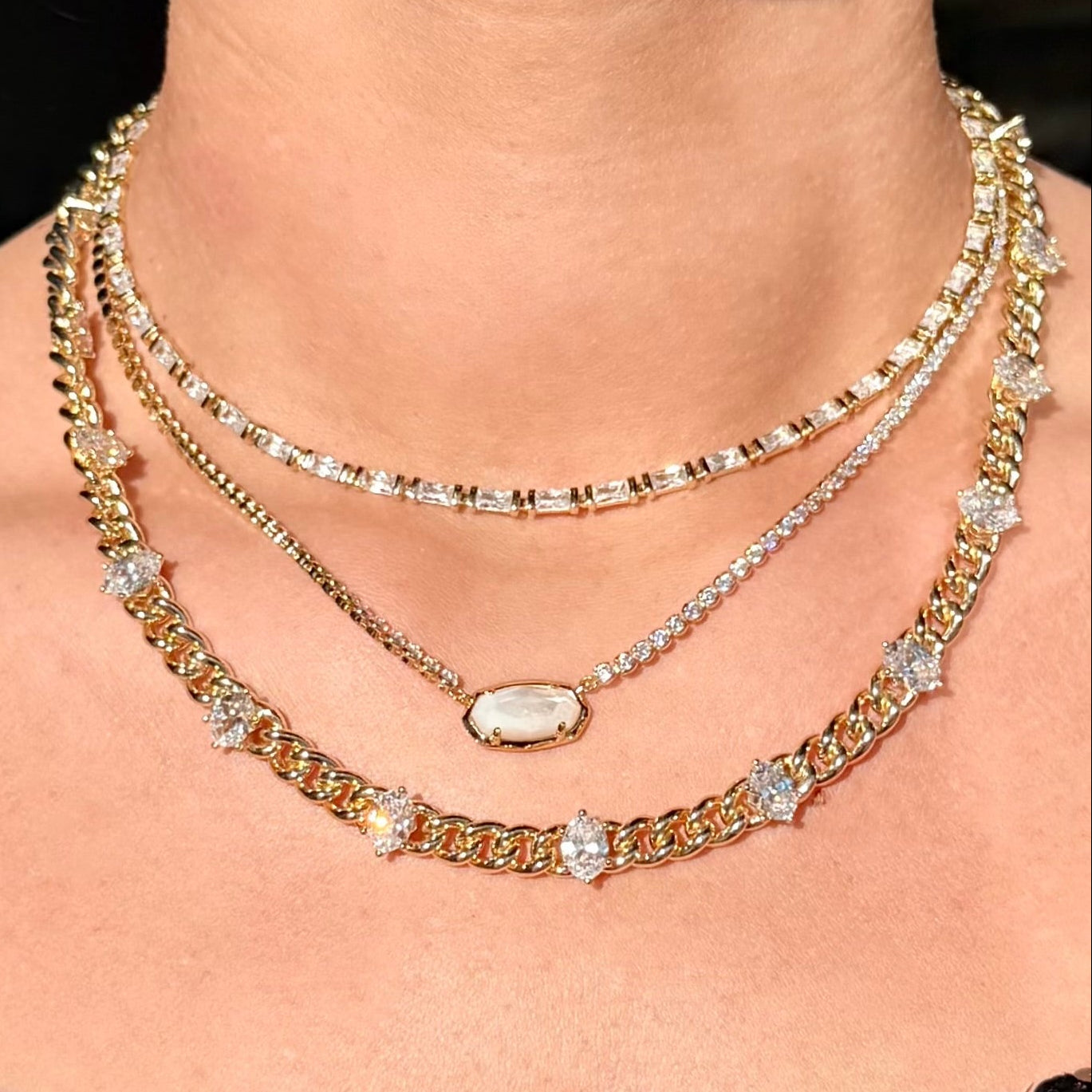 Close-up of a person wearing multiple gold necklaces with clear stones on a black background