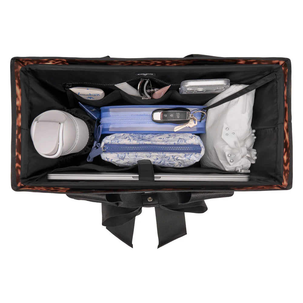 Open black handbag with various items including a blue pouch, white cup, and other small objects on a white background.