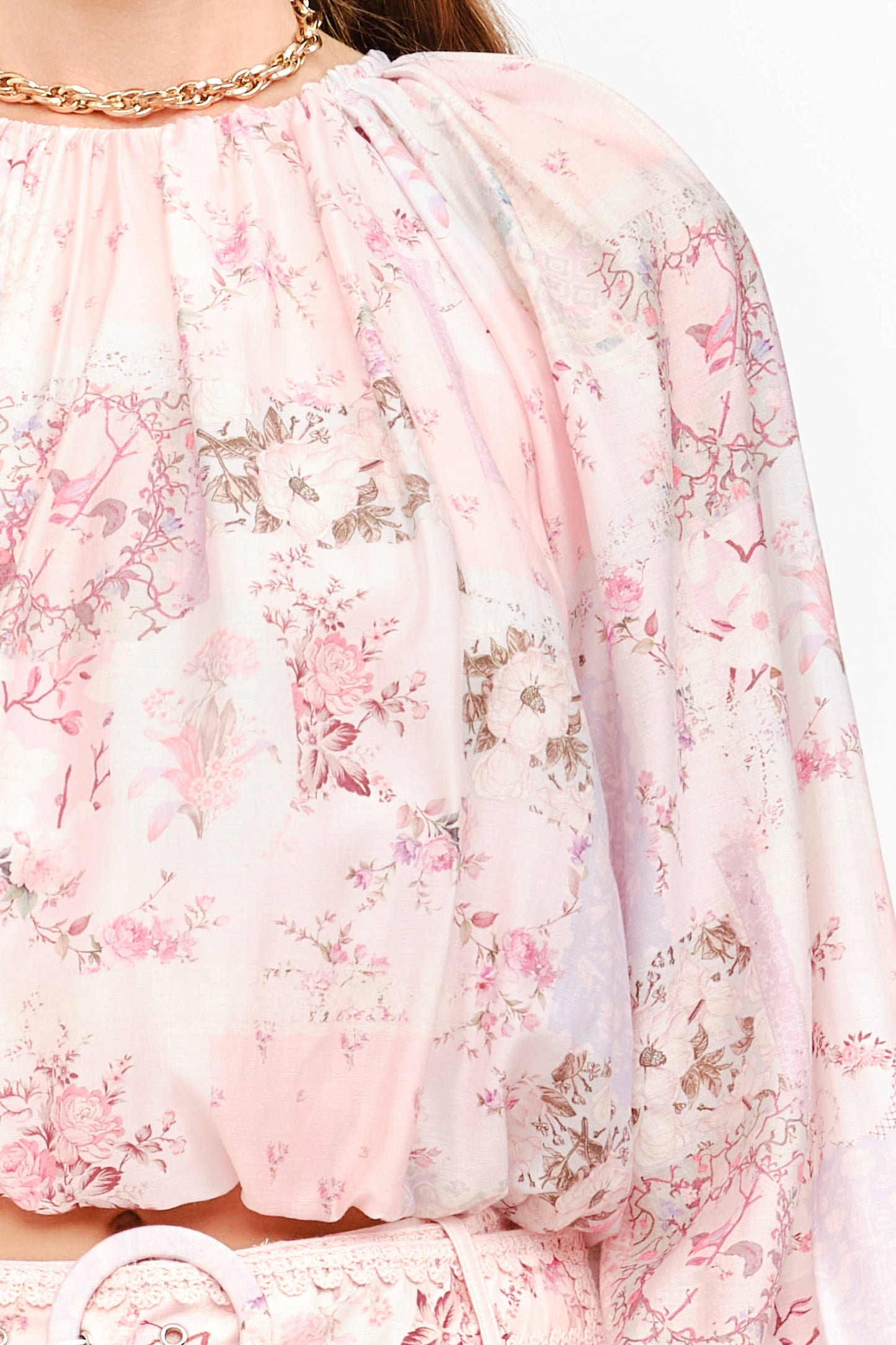 A close-up of a light pink sheer blouse with a delicate floral and bird print, featuring a gathered high neckline and long sleeves.