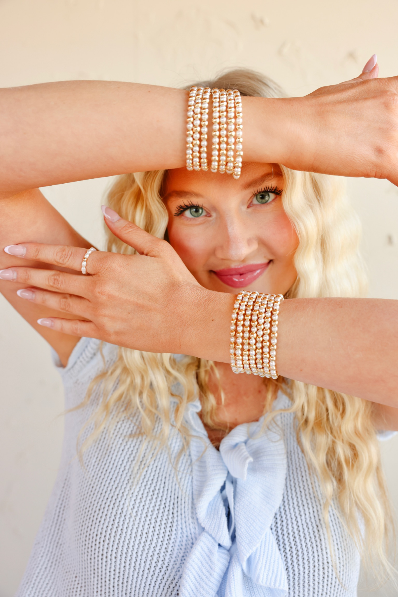 Woman wearing multiple pearl bracelets on a light background