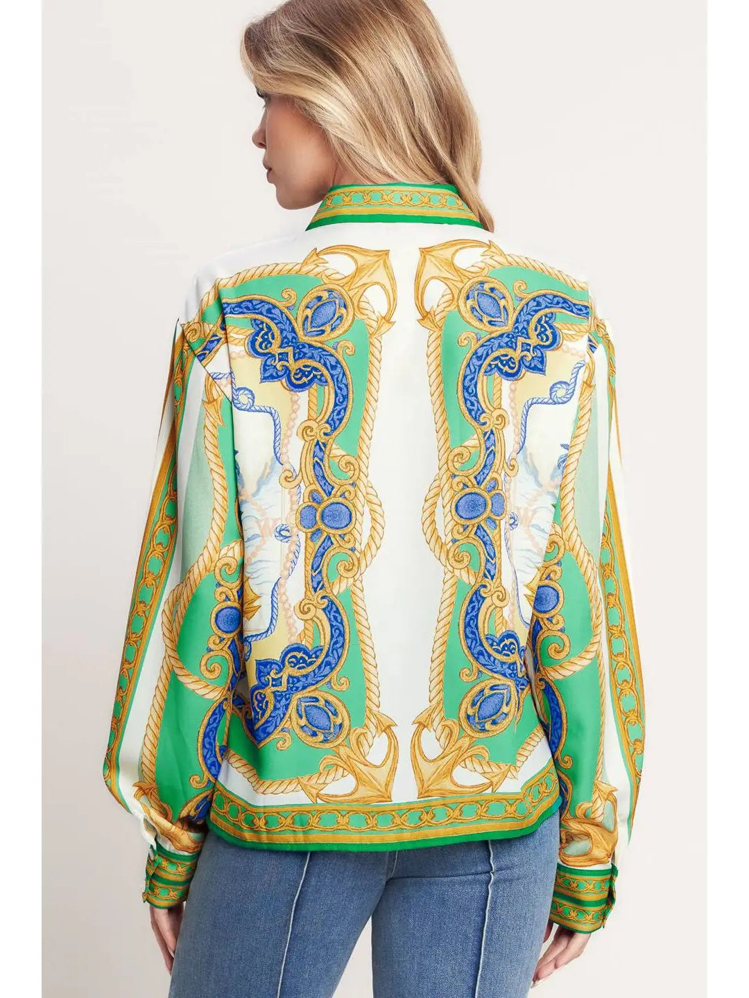 Woman wearing a patterned blouse with green, blue, and gold design on a plain background