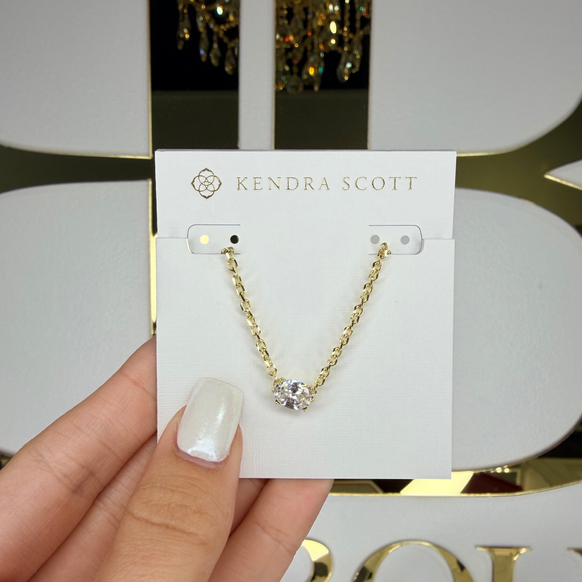 Gold necklace with a diamond held on a Kendra Scott card against a blurred background