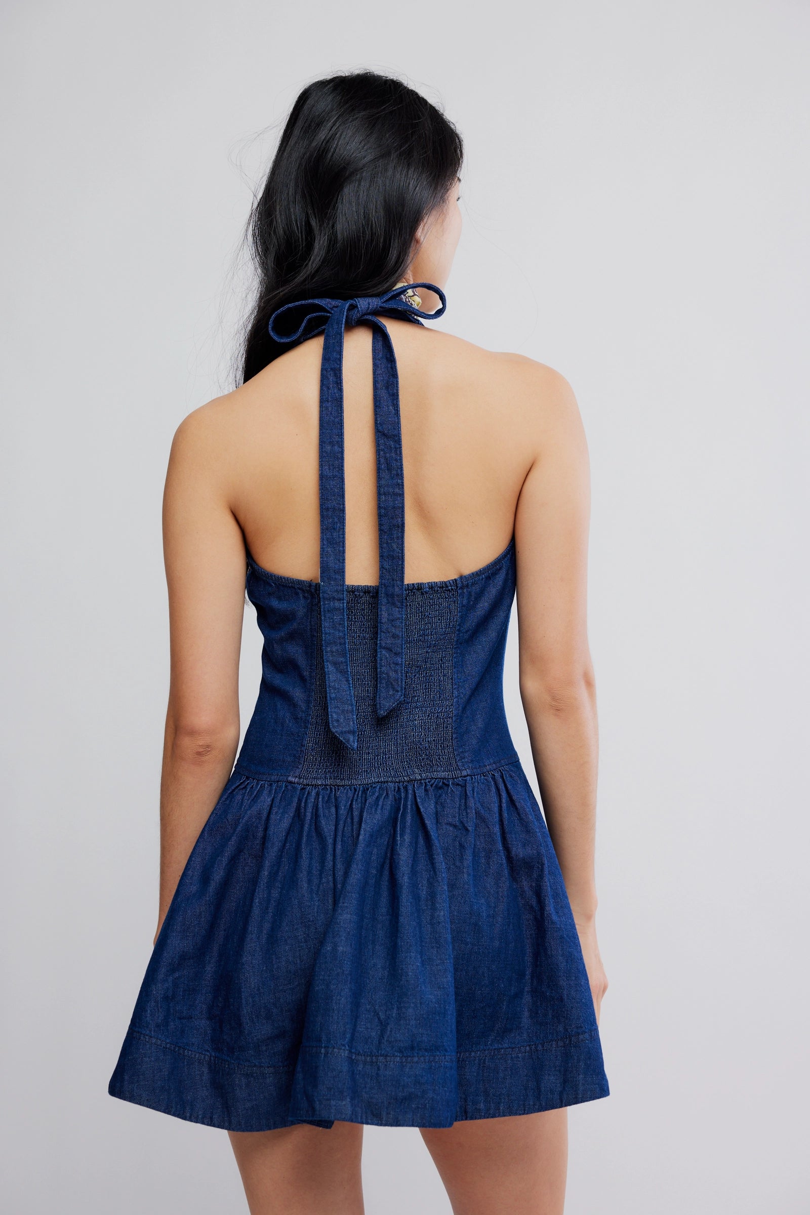 Woman wearing a blue denim dress with halter neck on a plain background