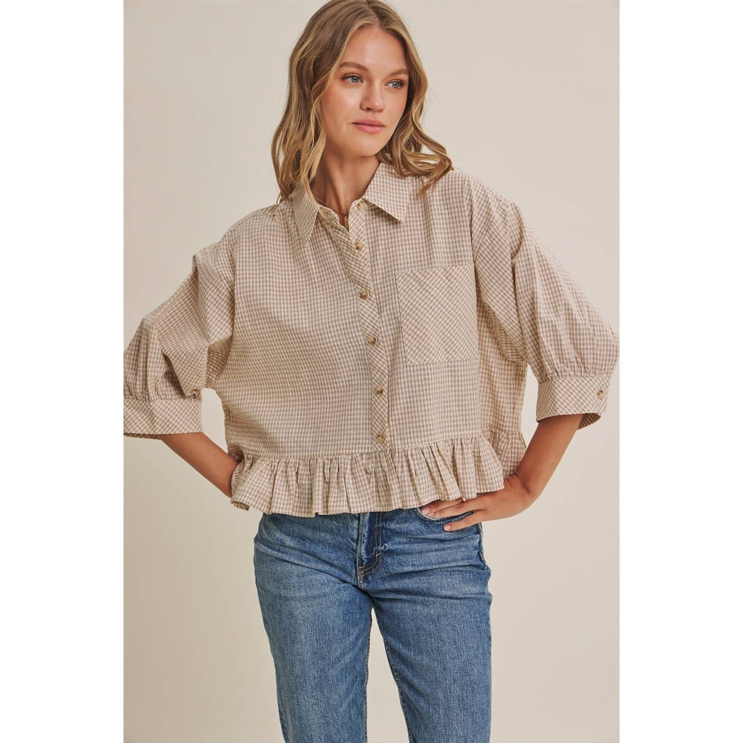Woman wearing a beige checkered blouse and blue jeans against a plain background