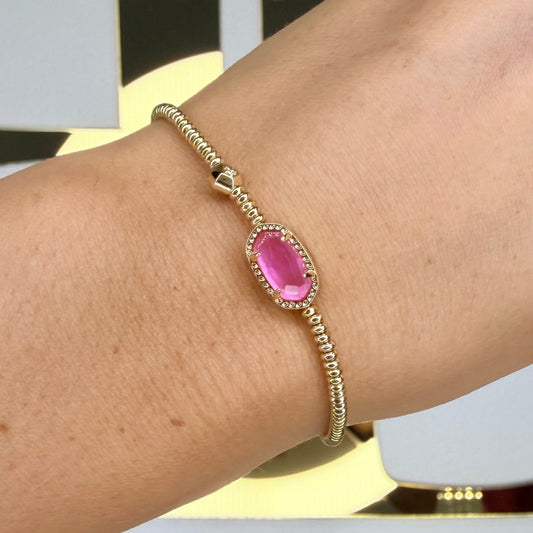 Gold bracelet with a pink gemstone on a blurred background