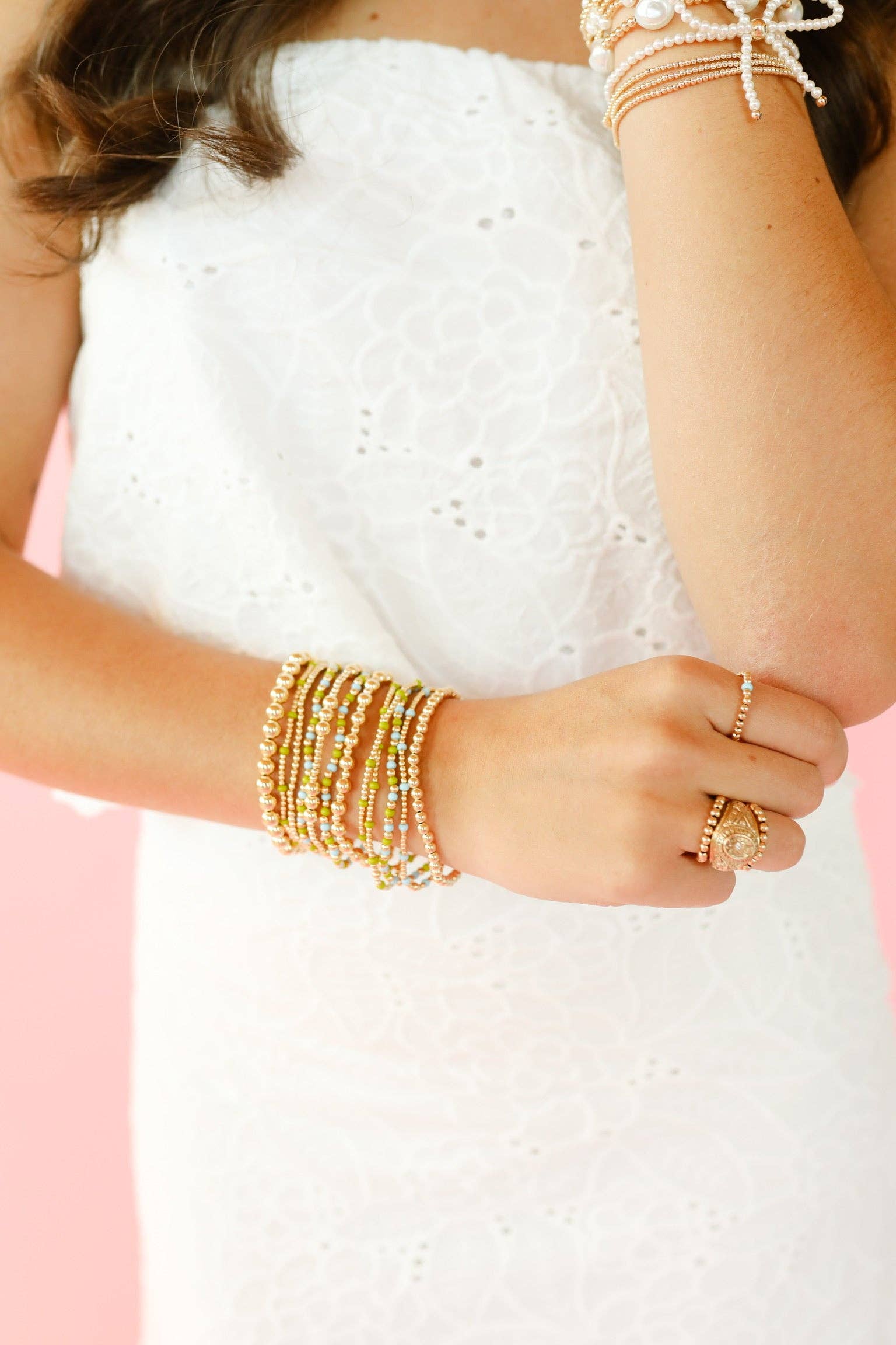 Close-up of a person wearing multiple pearl bracelets and rings on a white background