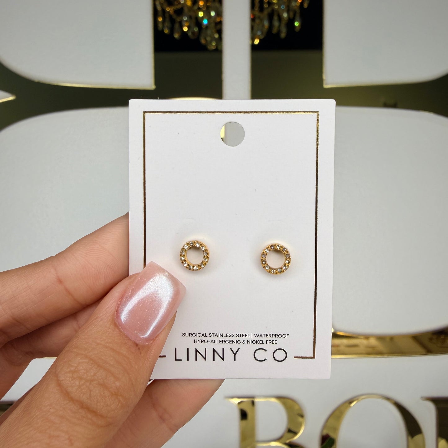 Gold hoop earrings on a Linny Co card held by a hand with a blurred background
