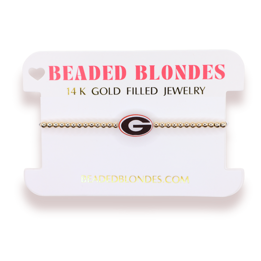 A gold beaded bracelet with a Georgia Bulldogs logo charm, displayed on a white branded card labeled 'BEADED BLONDES'.
