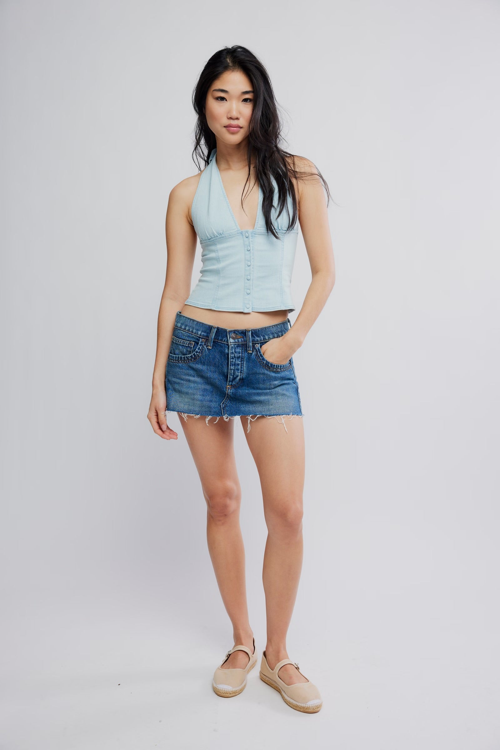 Woman wearing a light blue sleeveless top and denim shorts on a white background