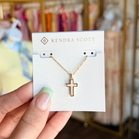 Gold necklace with a cross pendant on a Kendra Scott card held by a hand.
