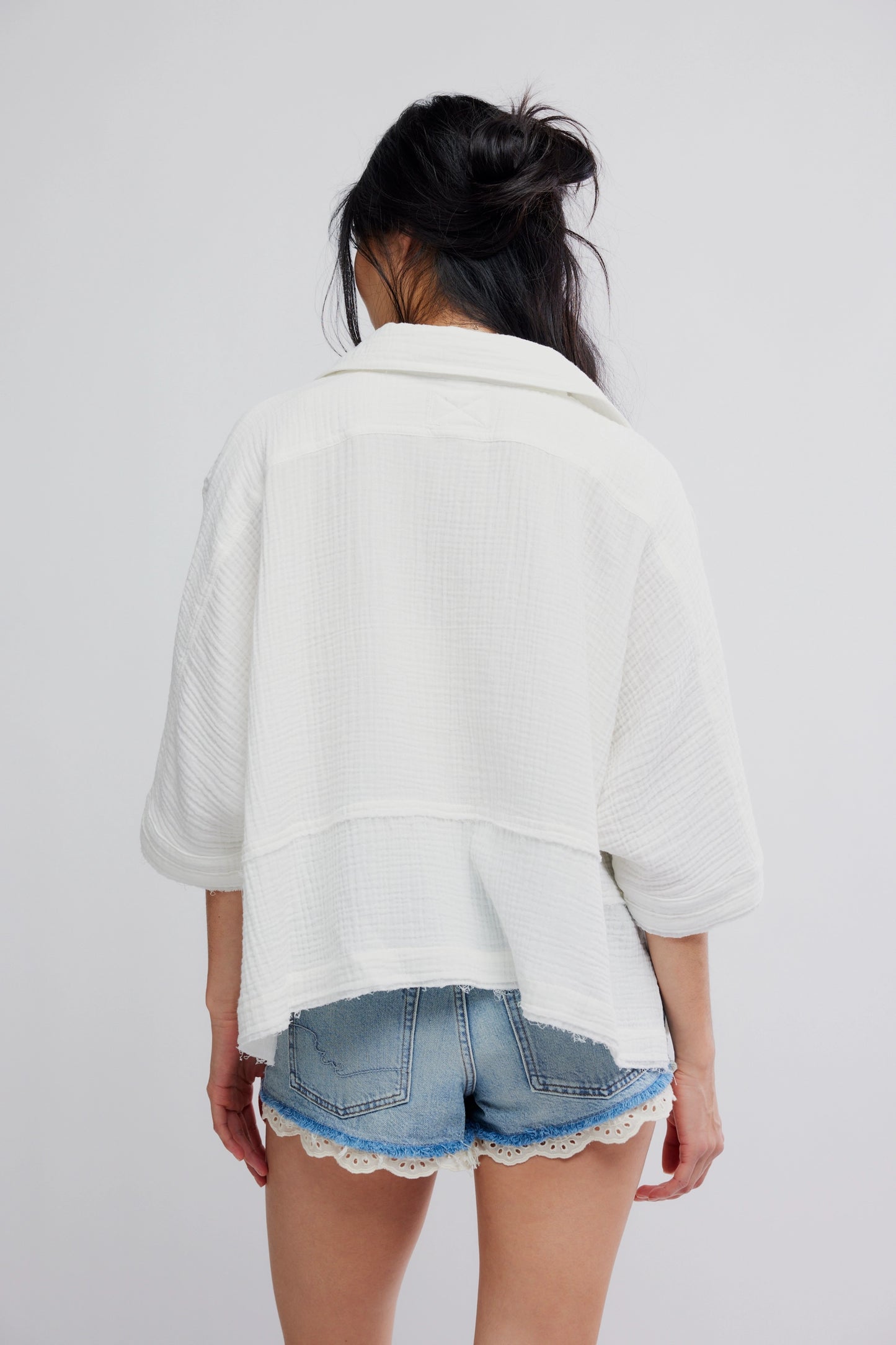 Person wearing a white oversized shirt and denim shorts with lace trim on a plain background