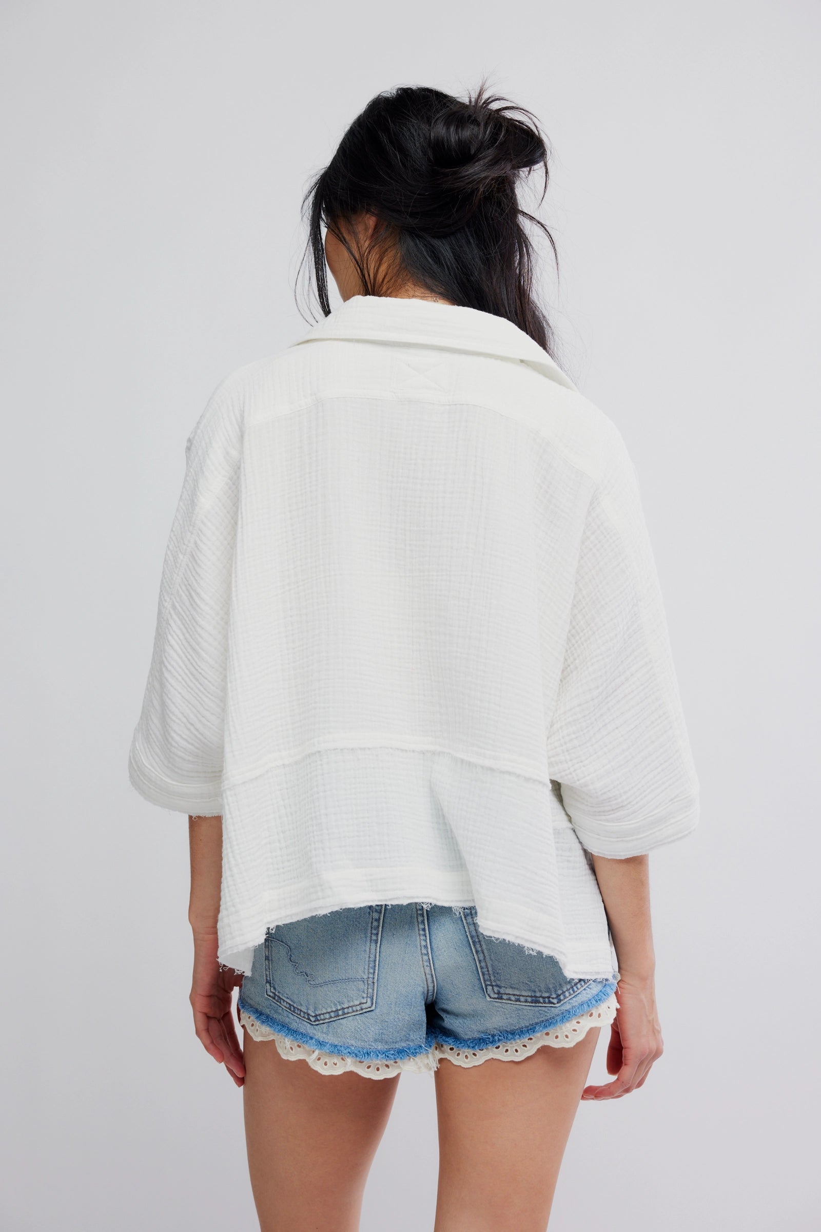 Person wearing a white oversized shirt and denim shorts with lace trim on a plain background