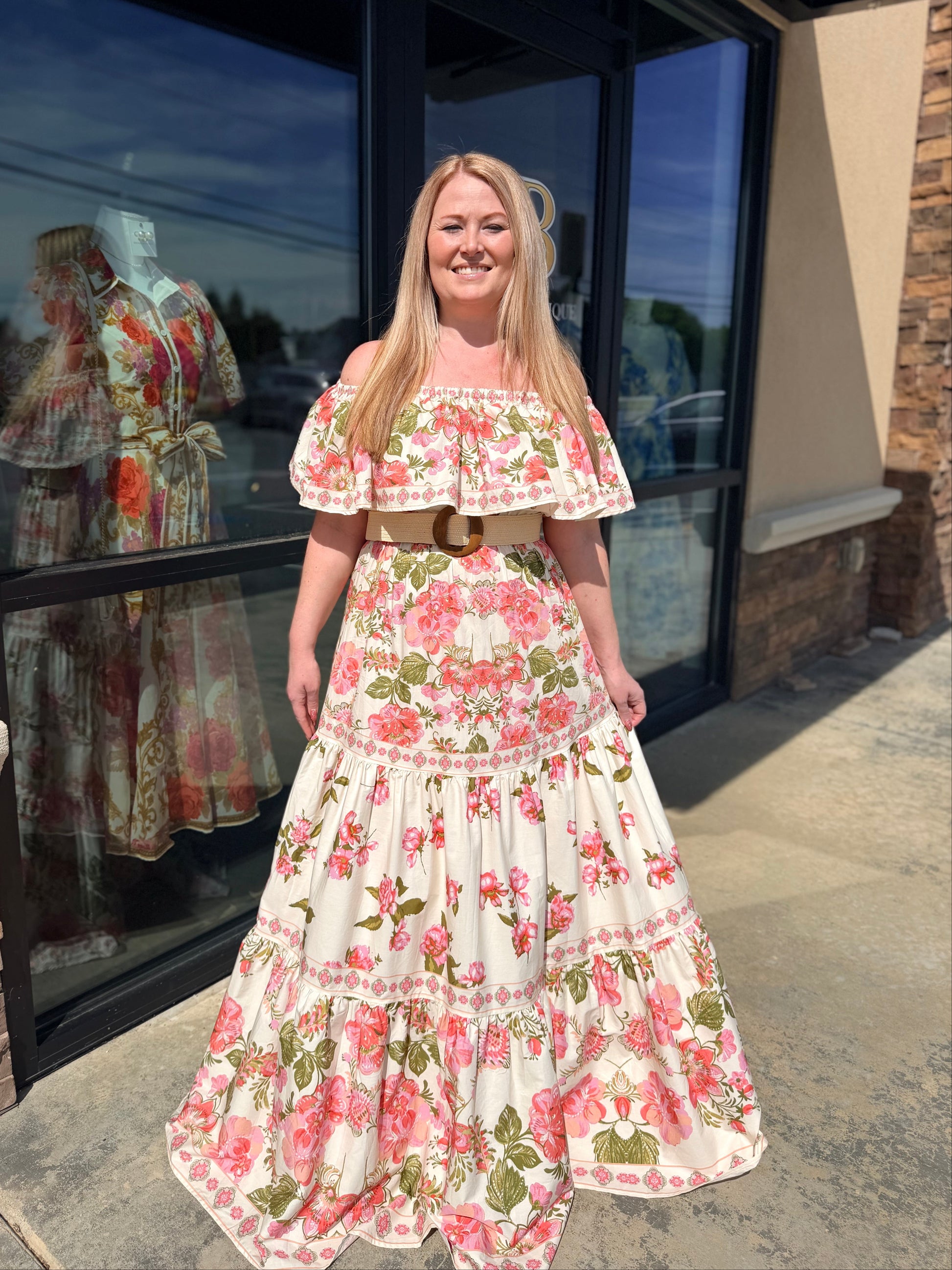Woman wearing a floral dress standing outside a store with a reflection of another floral dress in the window.