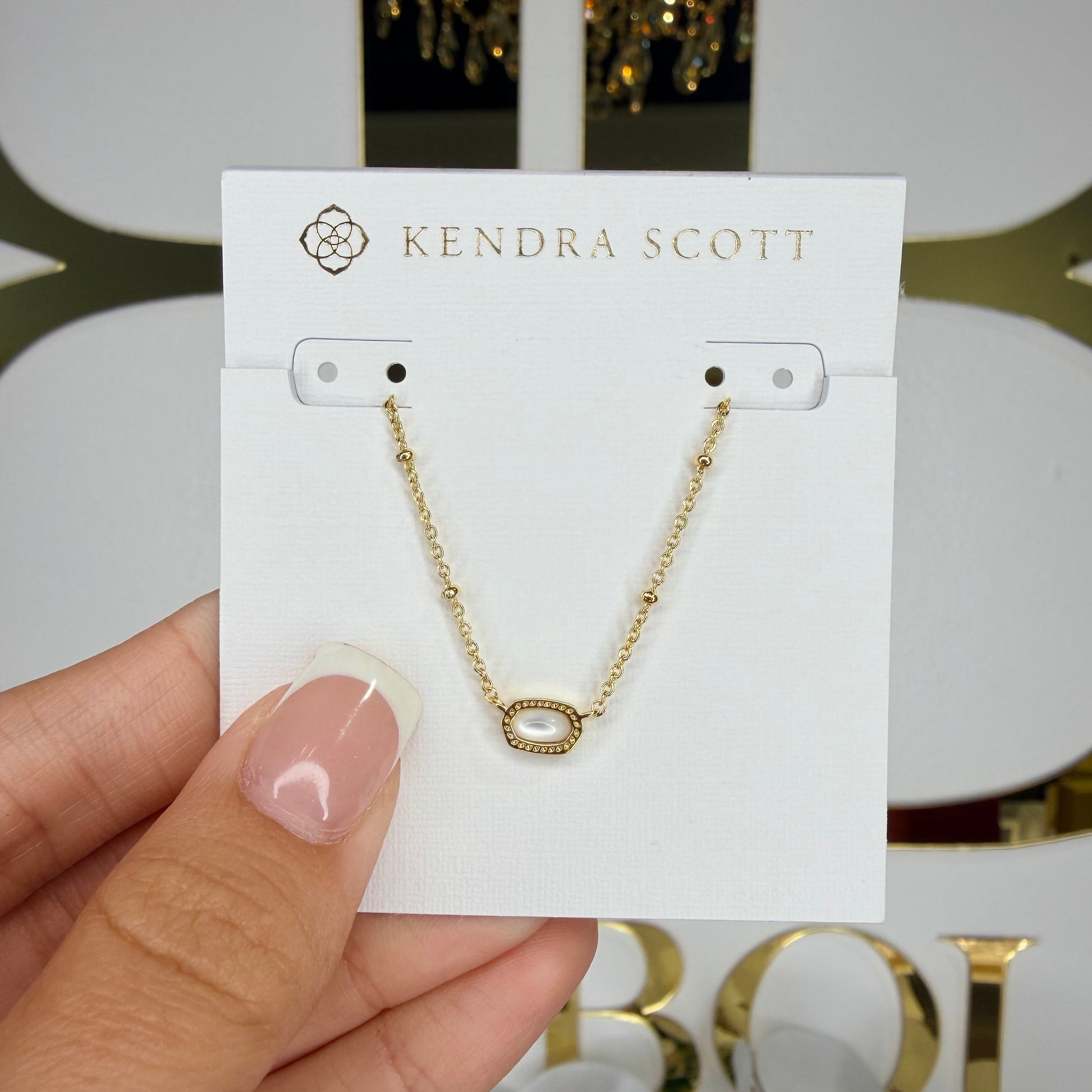 Gold necklace on a Kedra Scott card held by a hand with a blurred decorative background
