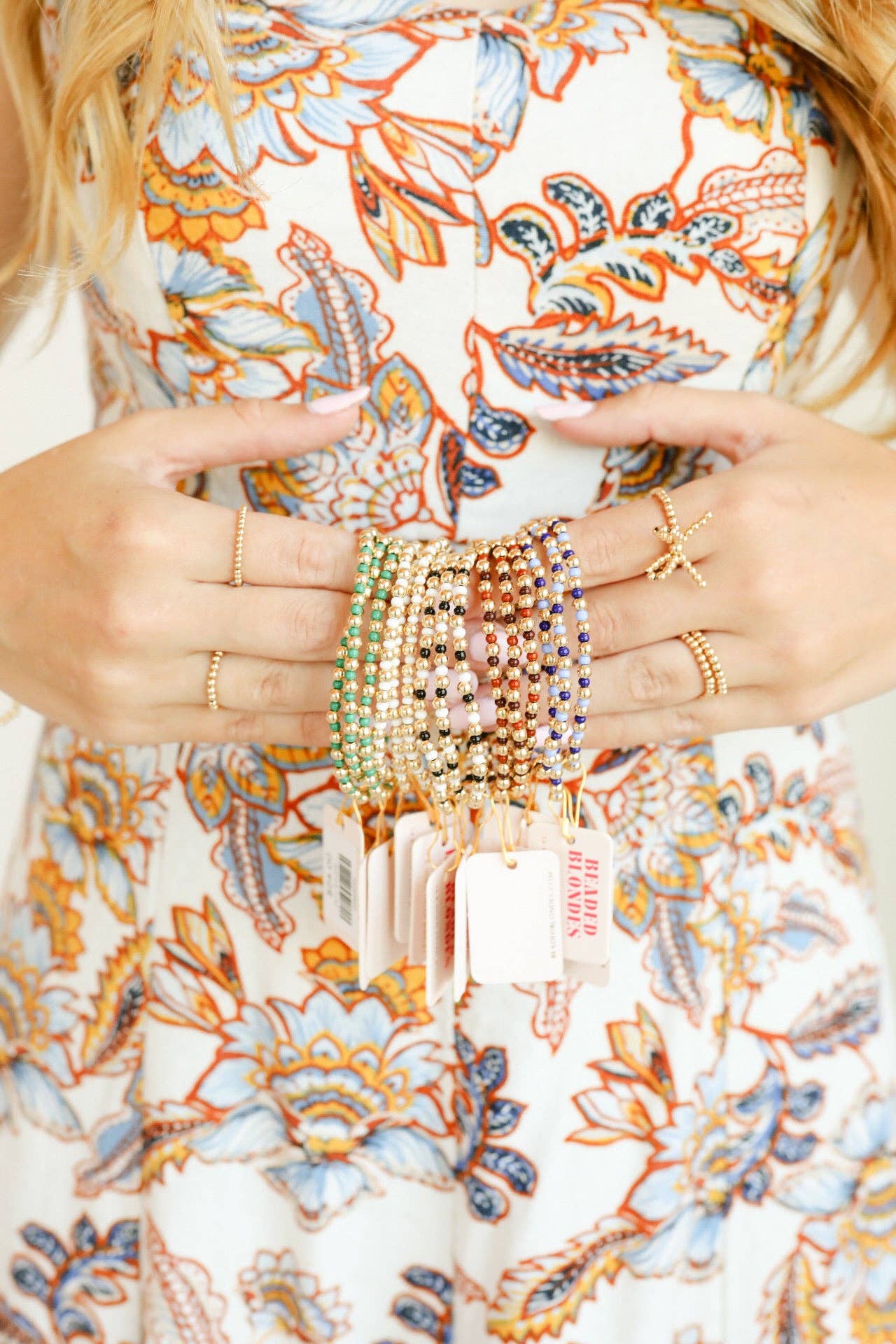 Close-up of hands wearing multiple bracelets and rings on a floral-patterned fabric background
