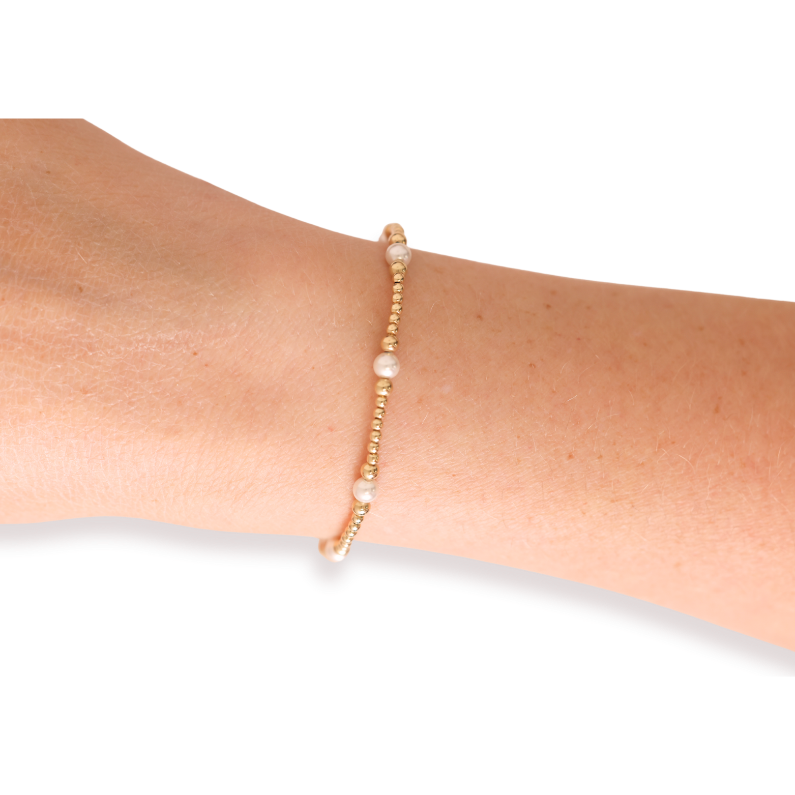 Gold bracelet with small beads on a wrist against a white background