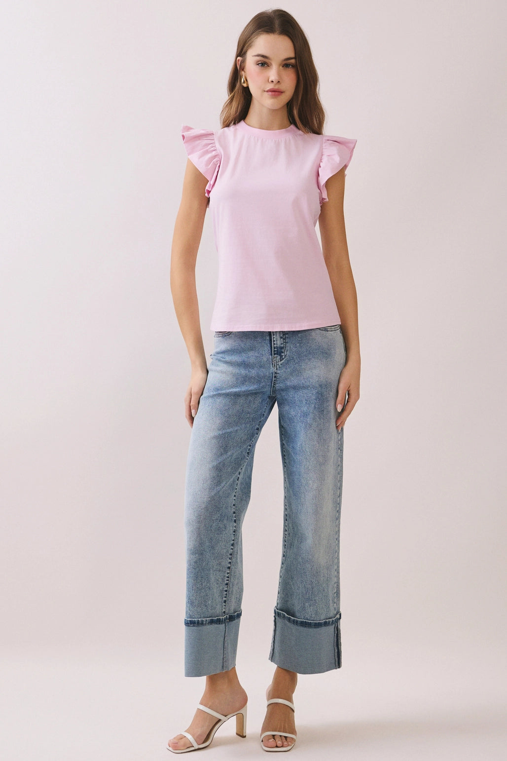 Woman wearing a pink top with ruffled sleeves and blue jeans on a light background