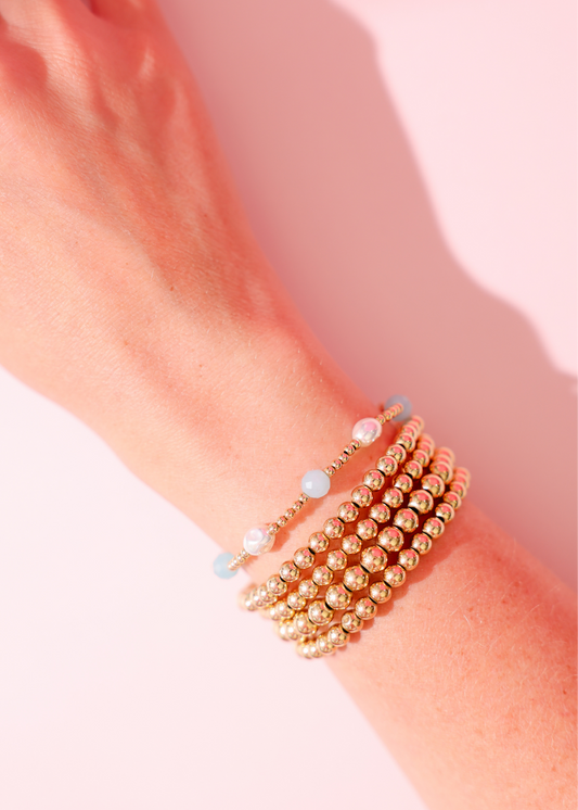 Close-up of a wrist wearing multiple beaded bracelets on a light pink background