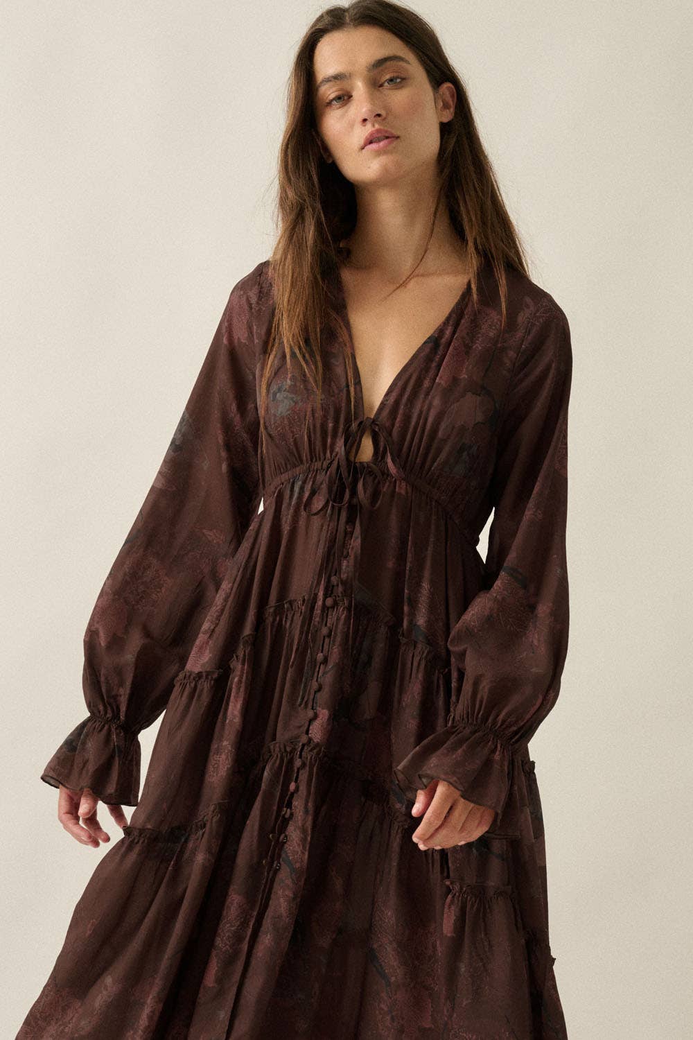 Woman wearing a brown dress with long sleeves against a plain background