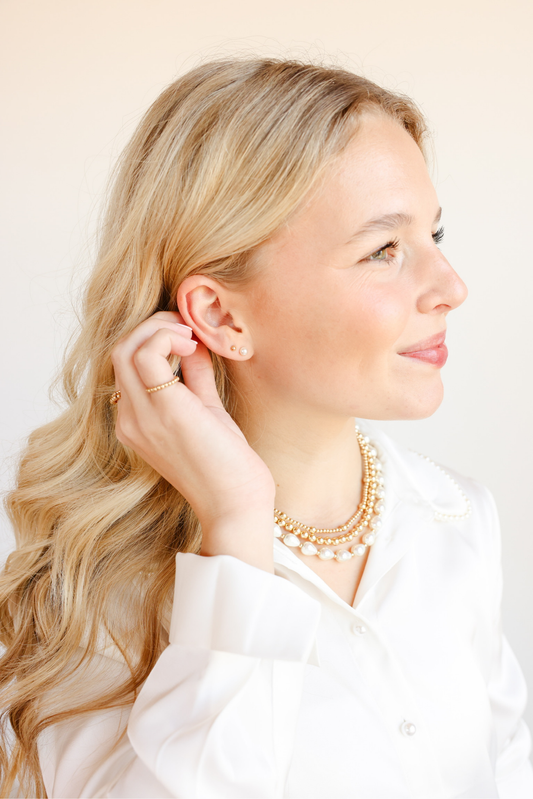 Woman wearing a gold necklace and earrings against a plain background