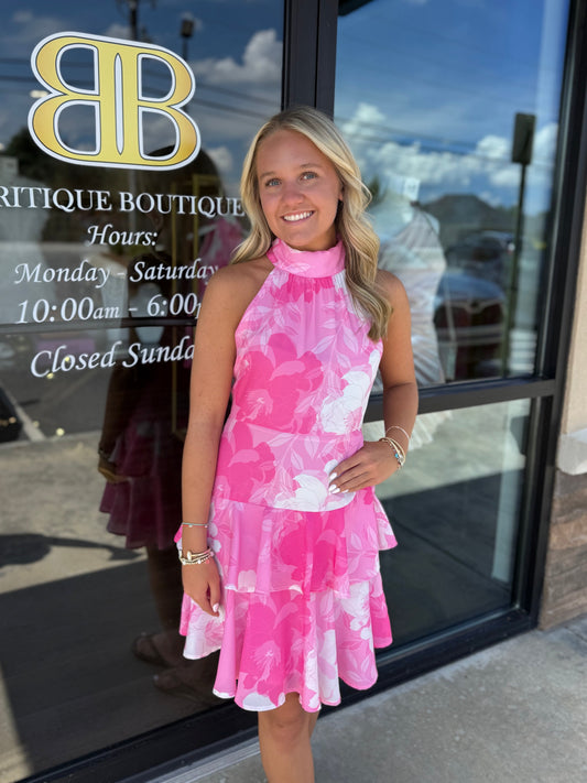 Britique Boutique model wearing pink floral mini ruffle dress in front of store front. 