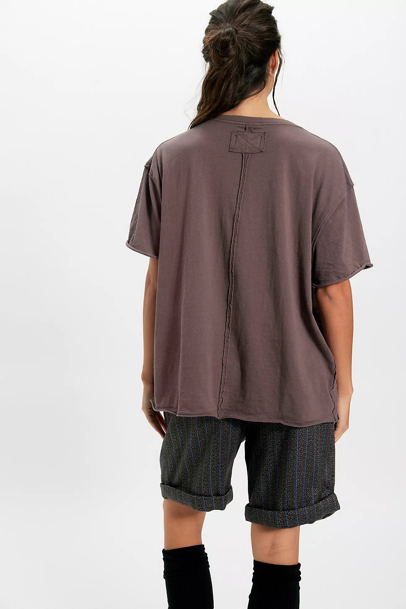 Person wearing a brown oversized t-shirt and dark shorts on a white background