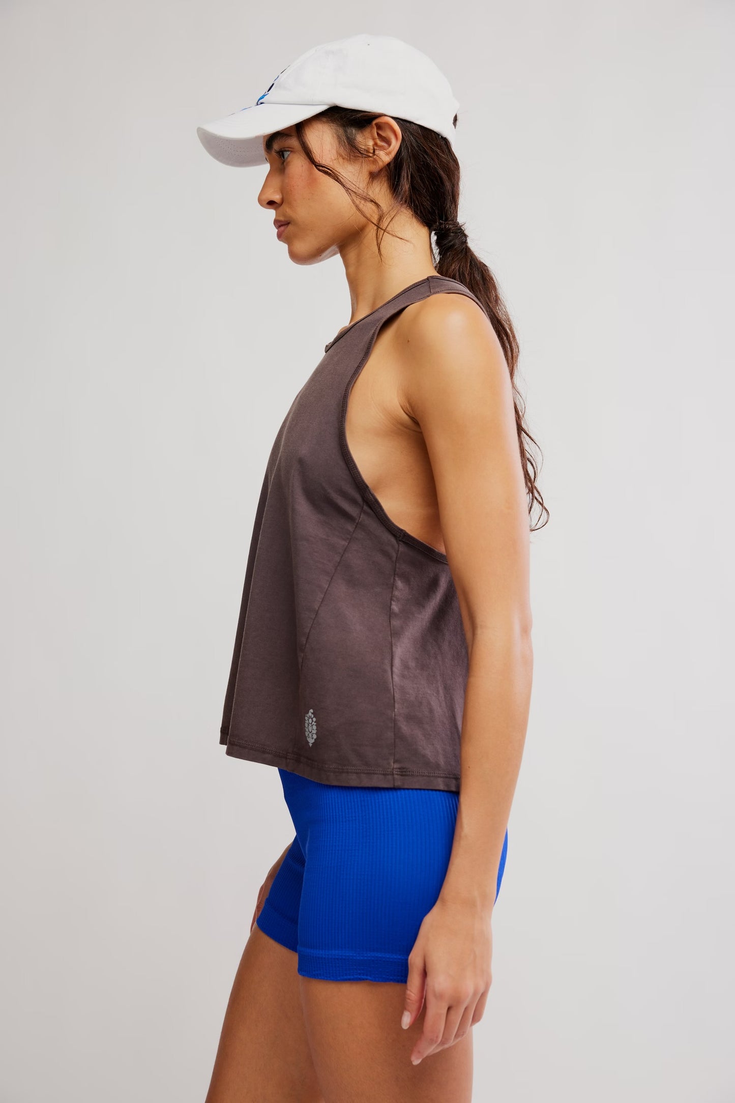 Woman wearing a brown tank top and blue shorts with a white cap on a light gray background