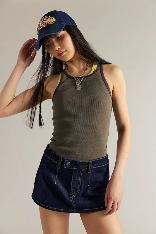 Woman wearing a green tank top and denim skirt with a blue cap on a neutral background