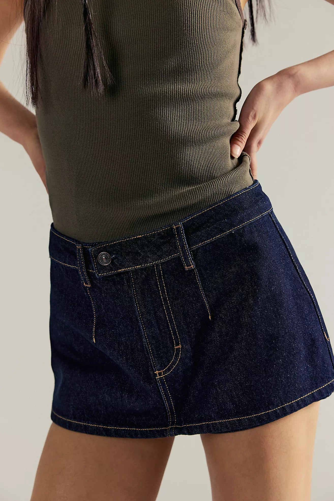 Person wearing a green top and dark blue denim skirt on a neutral background