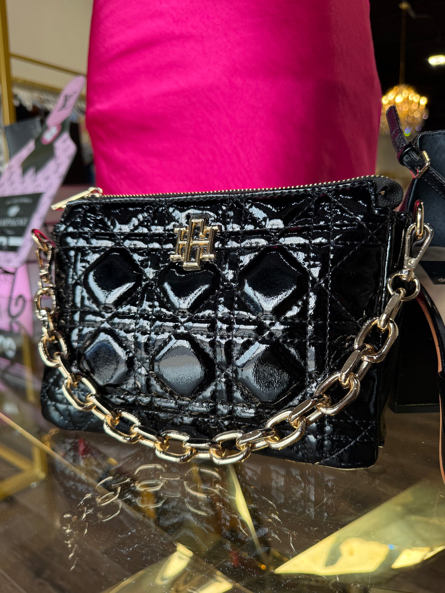 Black shiny purse with gold chain strap on clear table at BRITIQUE boutique 