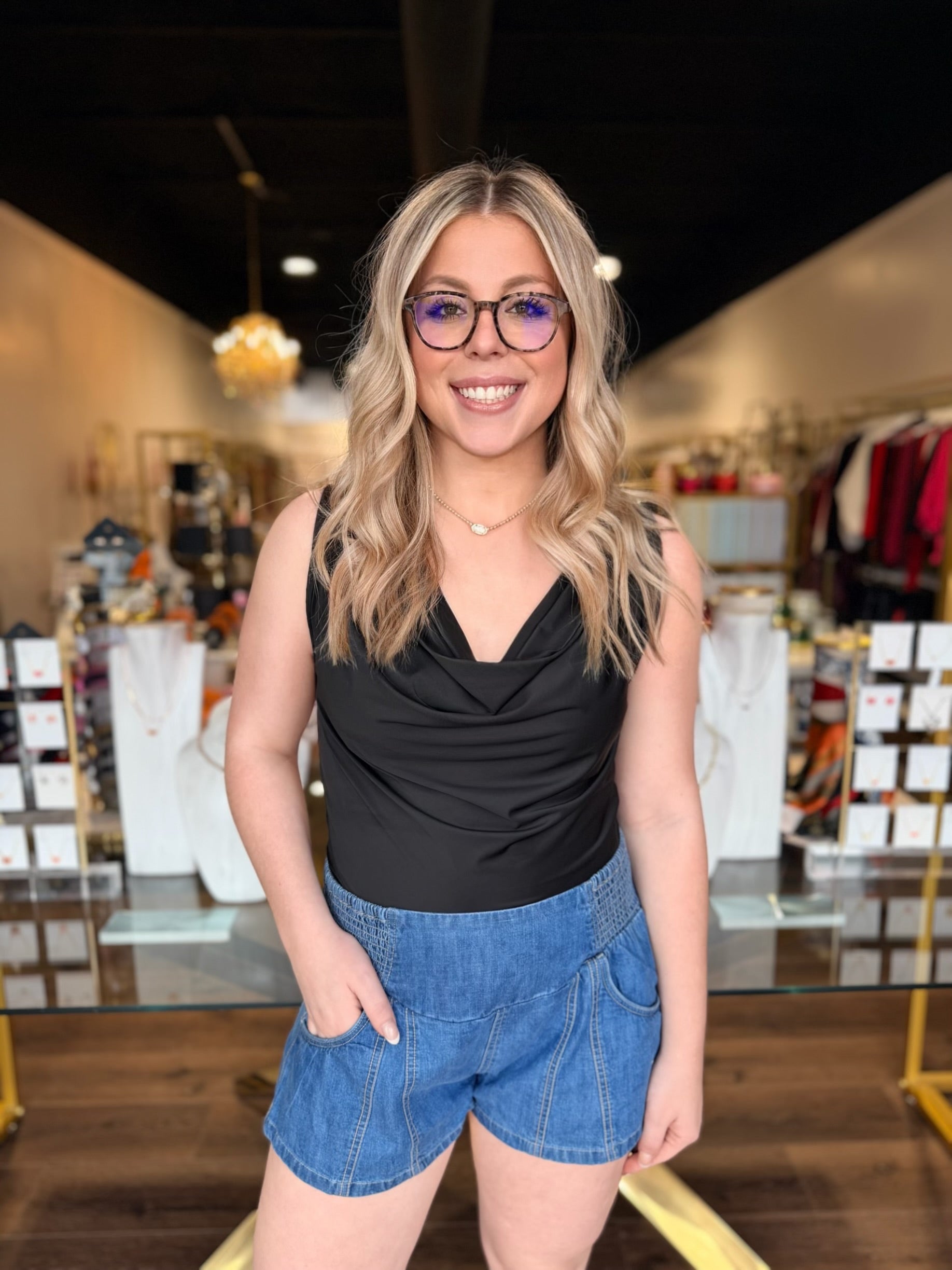 Woman wearing a black sleeveless top and blue shorts in a store setting