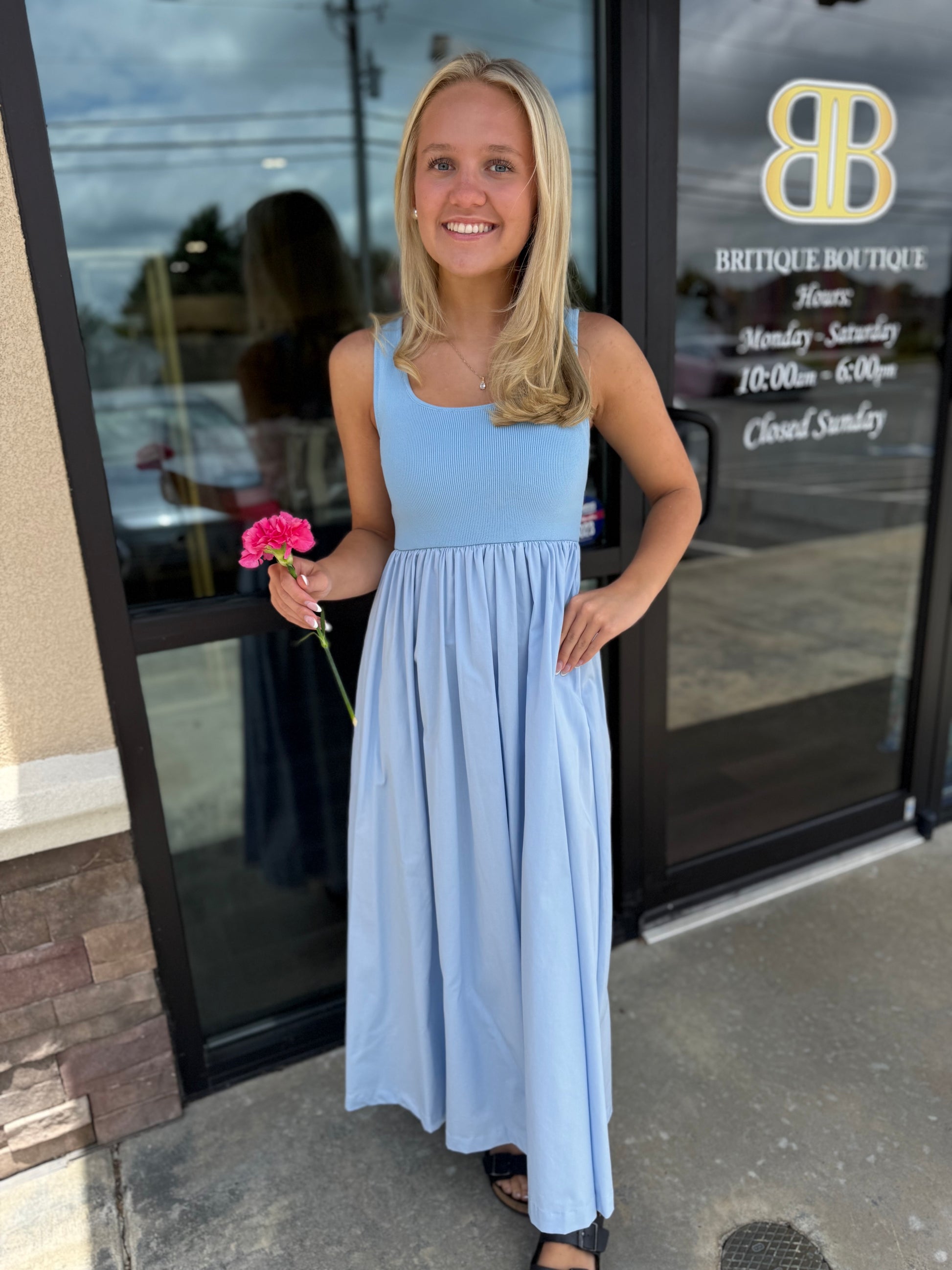 Britique Boutique model wearing blue midi dress holding flower in front of store windows 