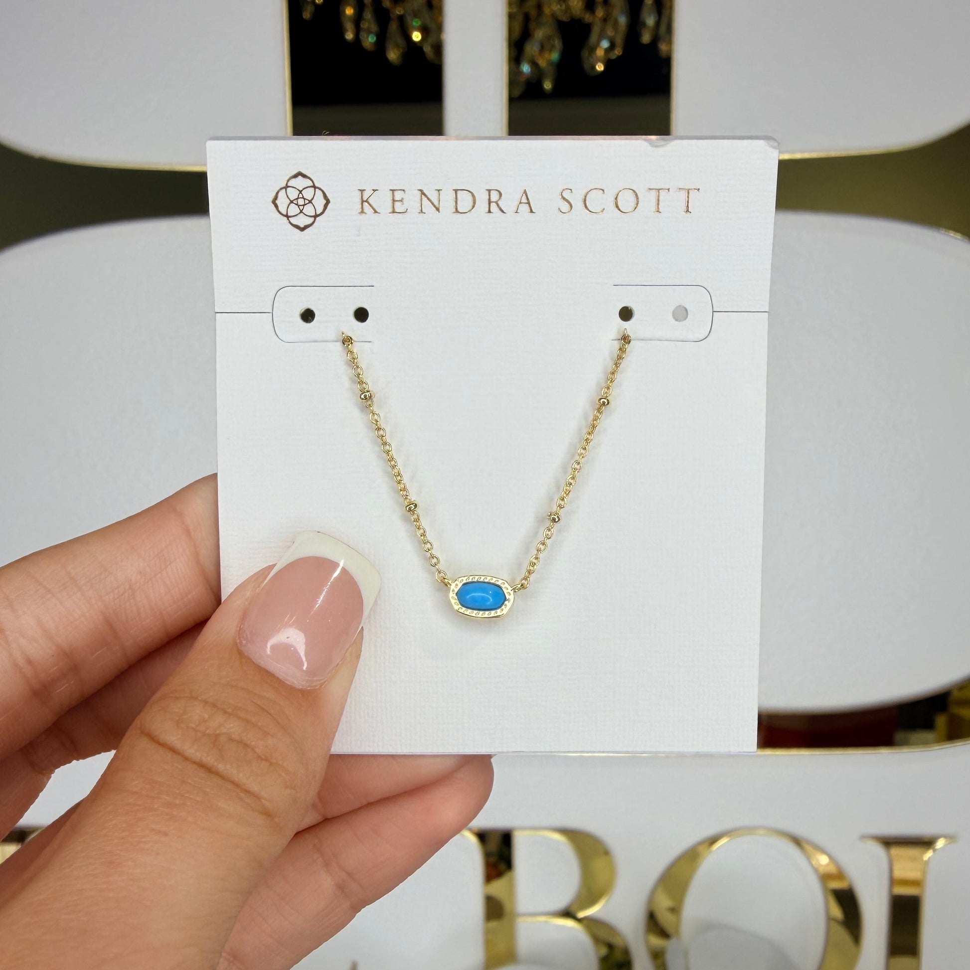 Kendra Scott earring on a card held by a hand with a decorative background