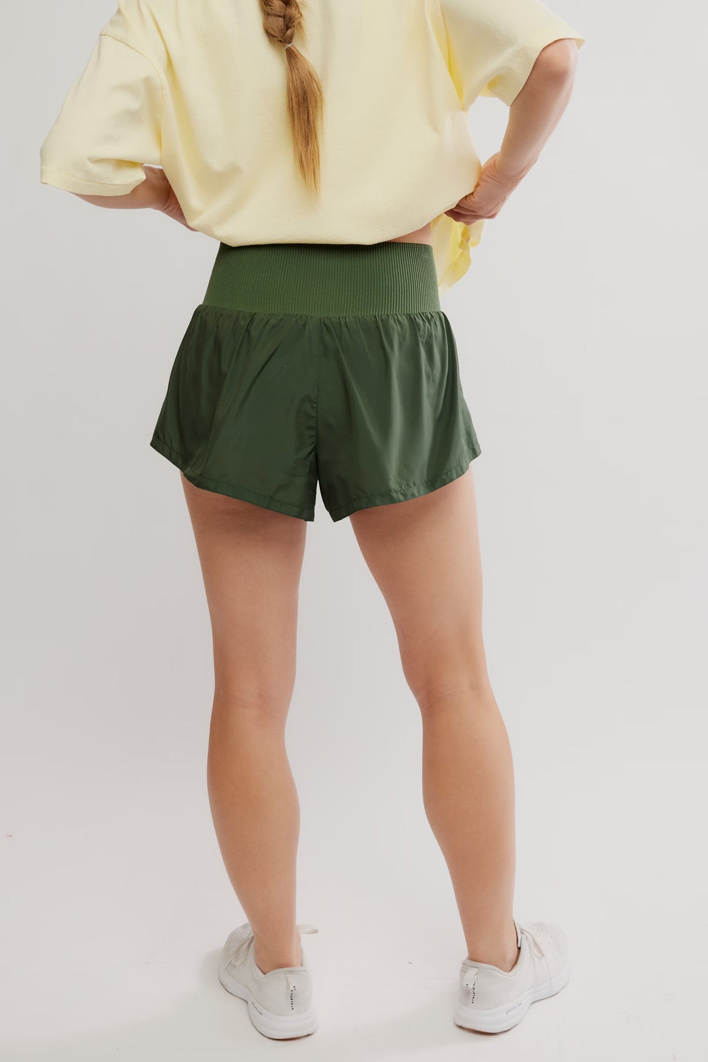 Person wearing green shorts and a yellow top on a plain background