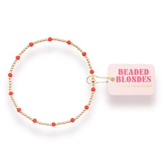 A gold-plated beaded bracelet with small red beads spaced along the chain, shown on a white background with a pink tag that reads 'BEADED BLONDES'.