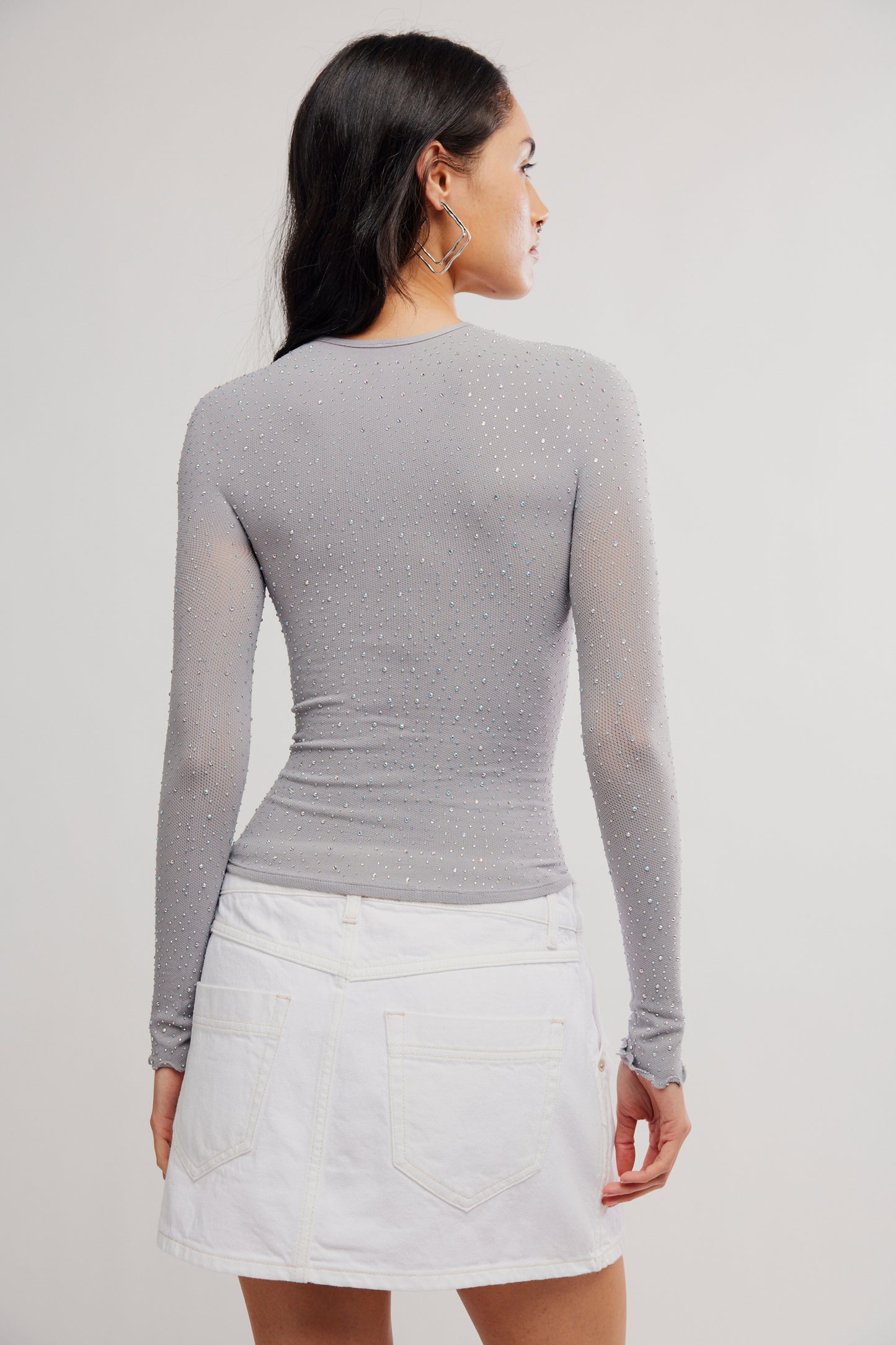 Woman wearing a gray long-sleeve top and white skirt on a plain background