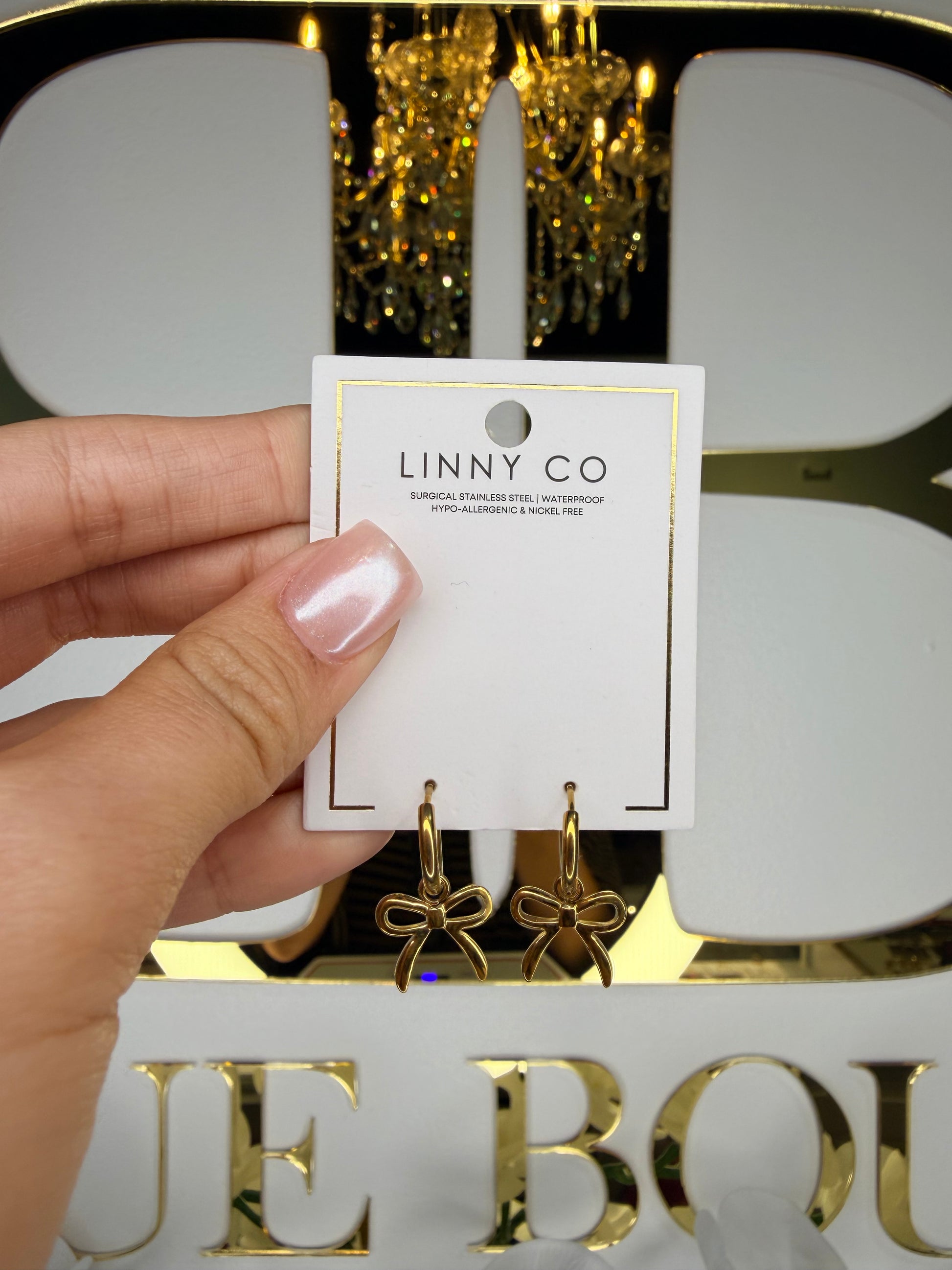 Hand holding a LINNY CO card in front of a gold and black decorative background