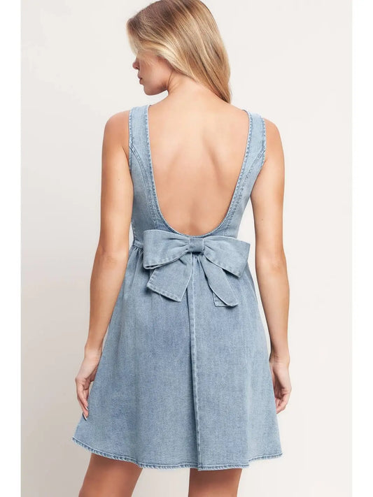 Woman wearing a light blue denim dress with a bow detail on a plain background