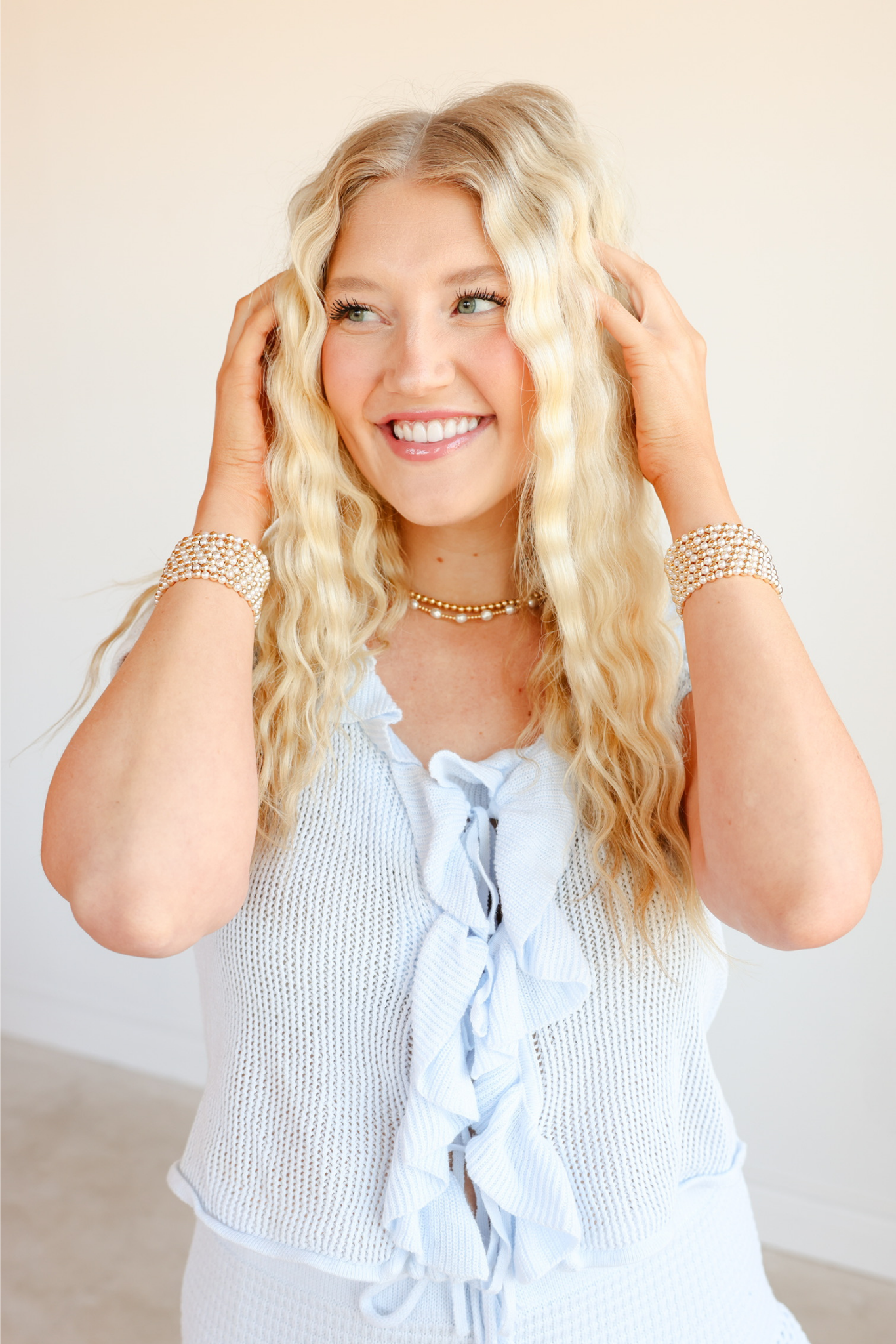 Woman with long blonde hair wearing a light blue sleeveless top against a plain background