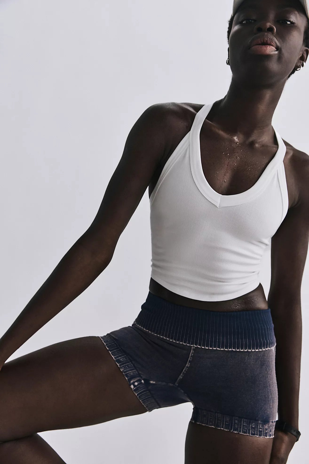 Person wearing a white tank top and dark shorts on a plain background